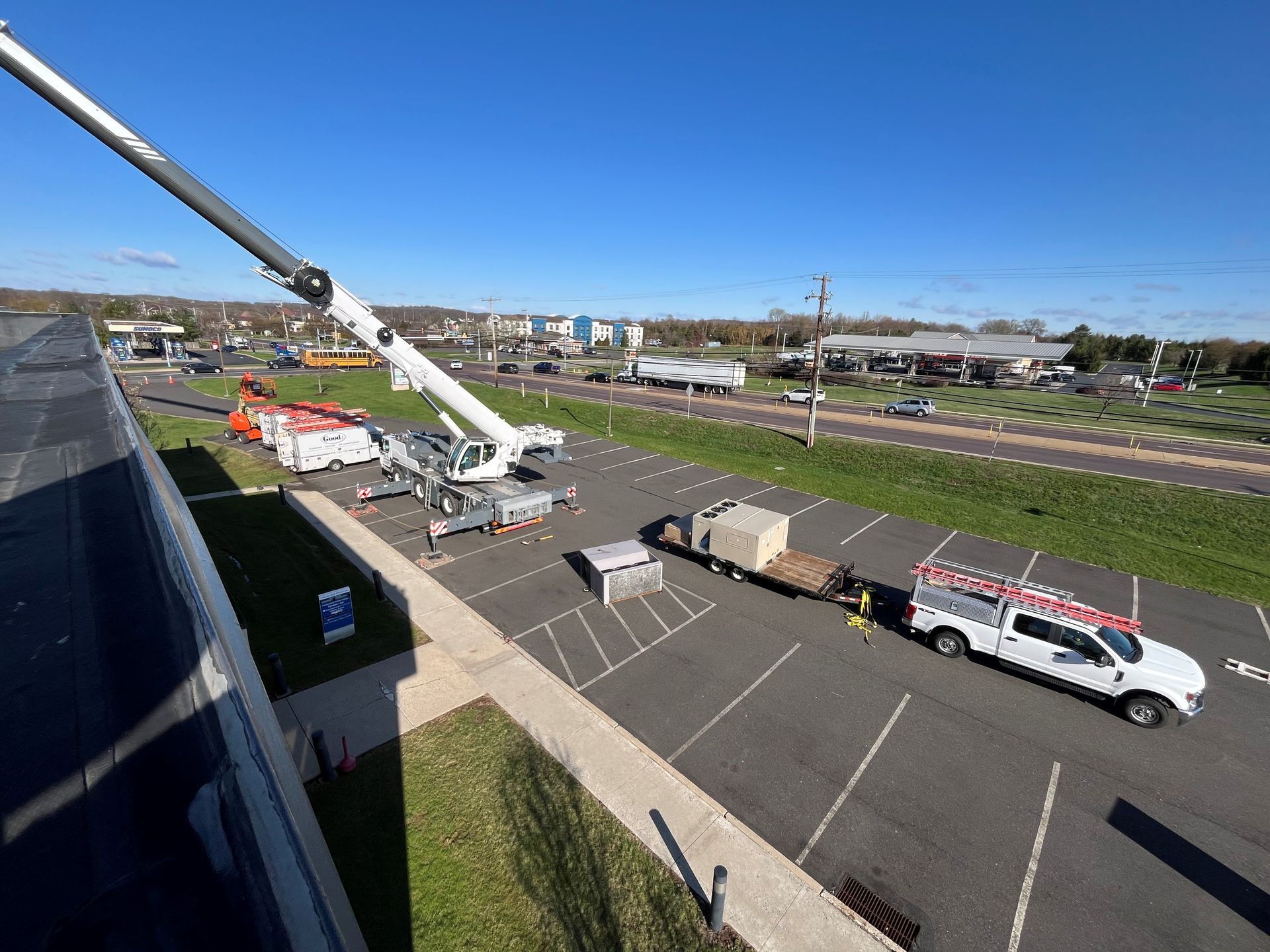 Crane lifting equipment near a building and parked truck on a sunny day.