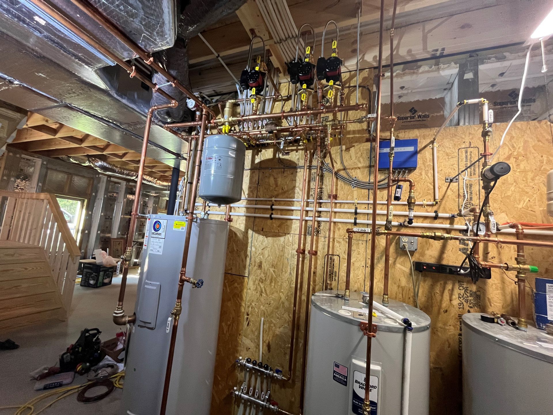 Copper pipes, tanks, and valves installed on a wood-paneled wall in a construction site.