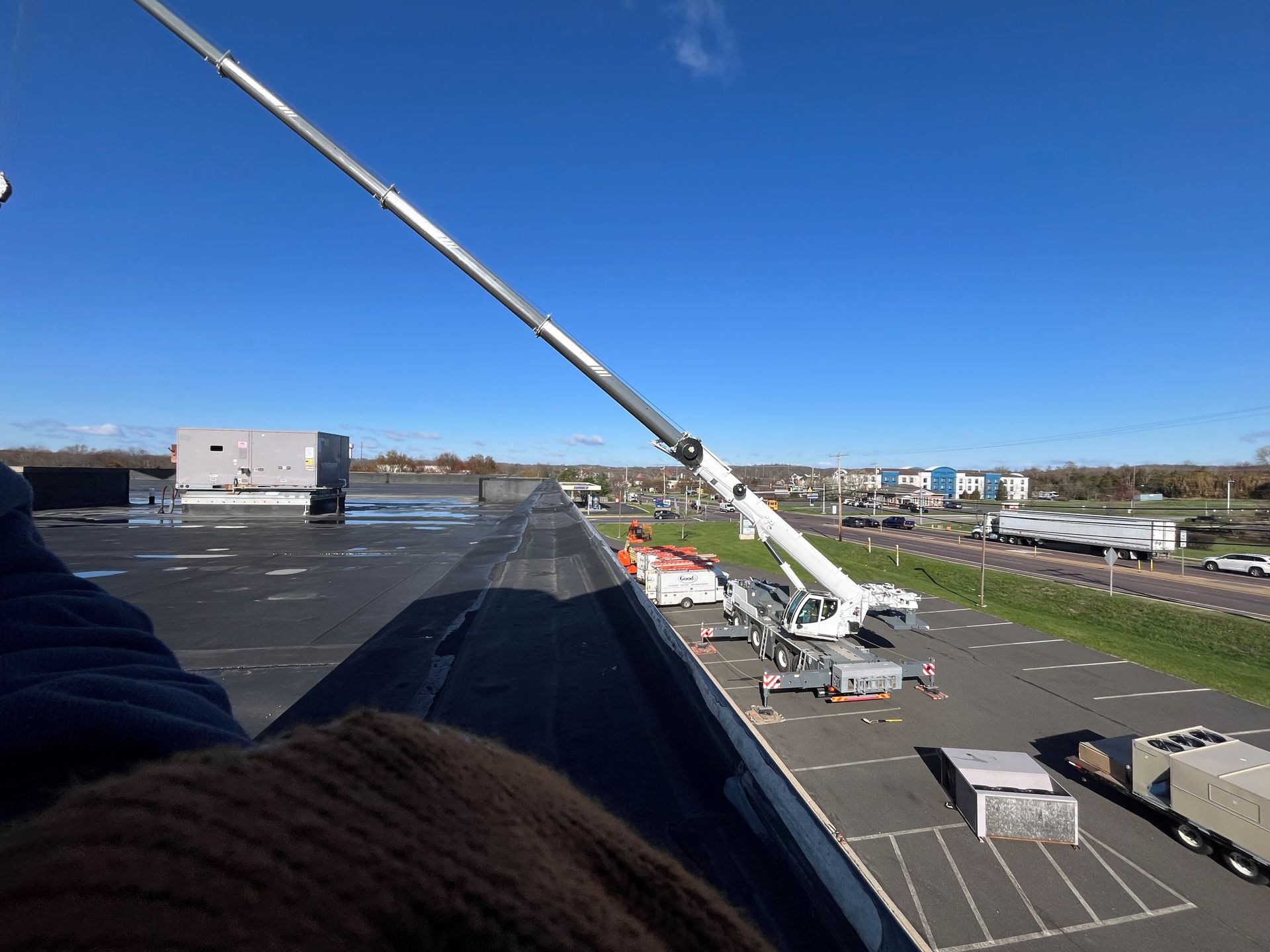 Crane extending over a flat roof, used for construction. Bright blue sky overhead.