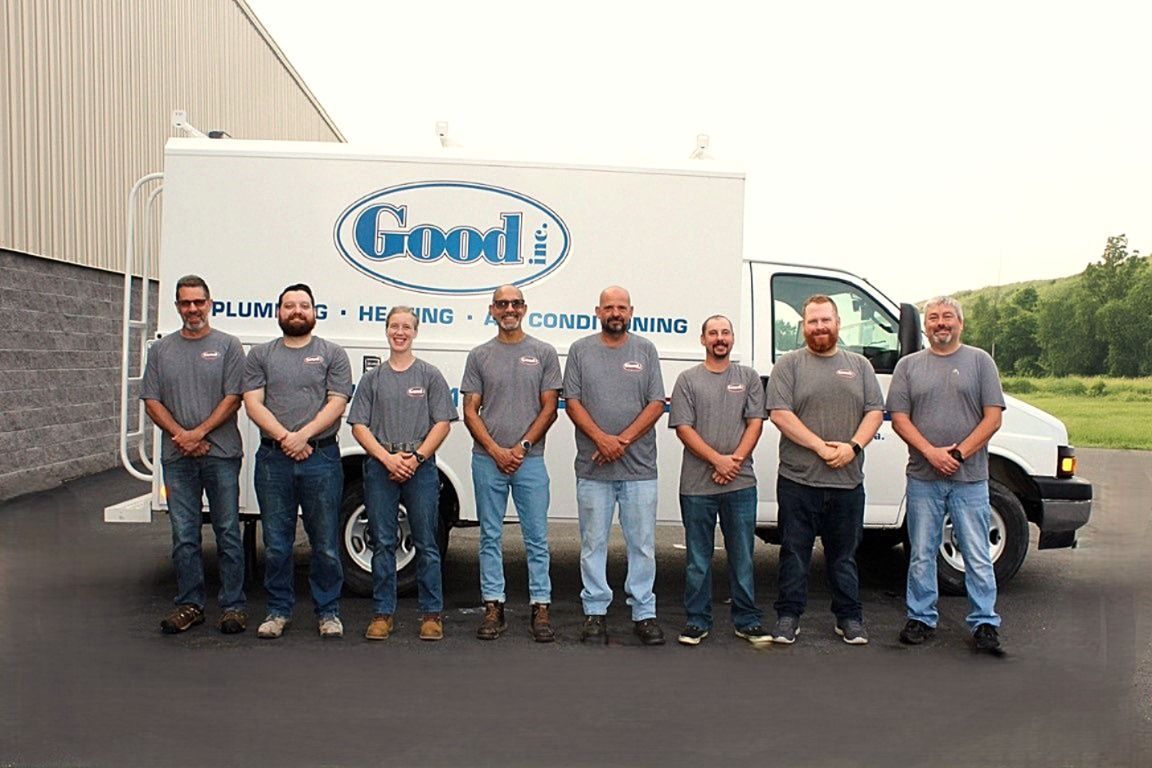 Group of eight men in front of a white service truck, smiling. 