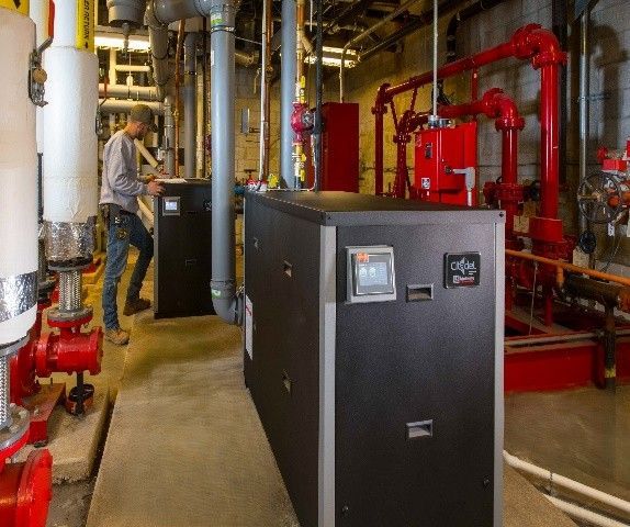 Man inspecting equipment in an industrial setting with black machines, red pipes, and insulation.