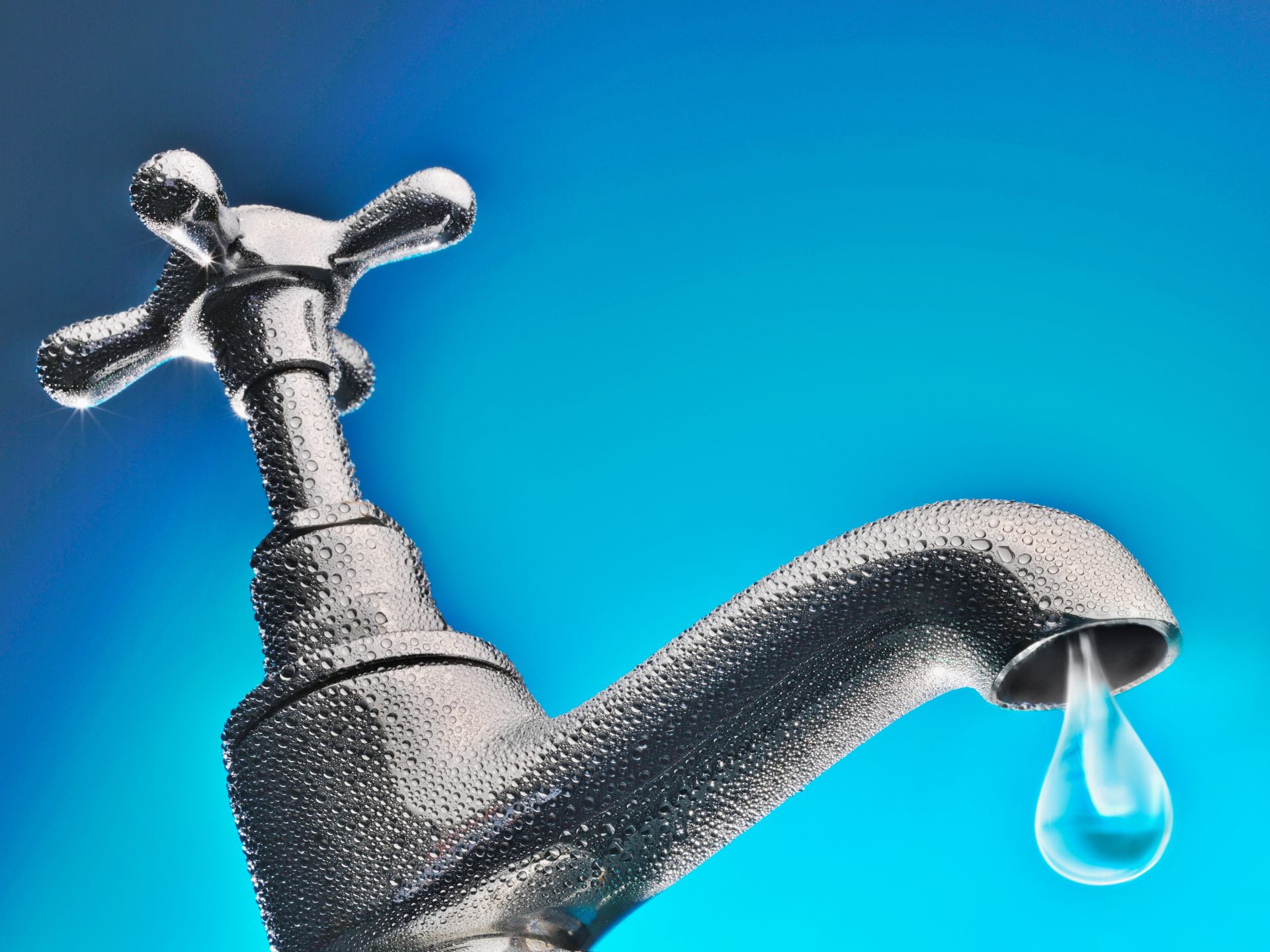 Chrome faucet with a water droplet against a blue background.