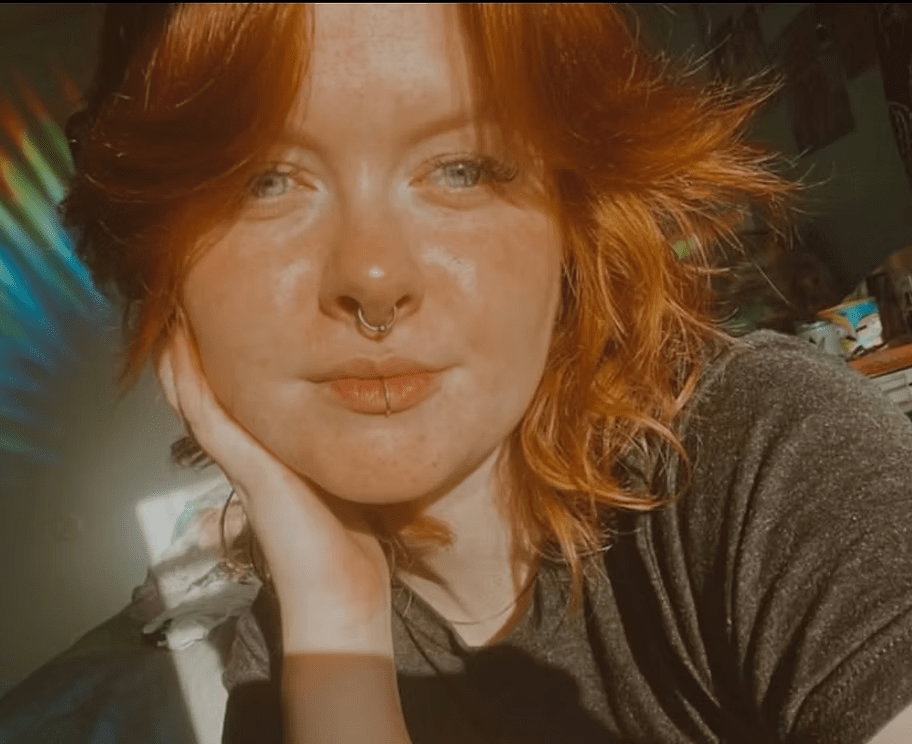 A woman with red hair is taking a selfie with her hand on her face.
