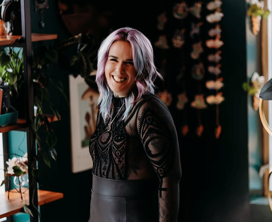 A woman with purple hair and a black top is standing in a room.