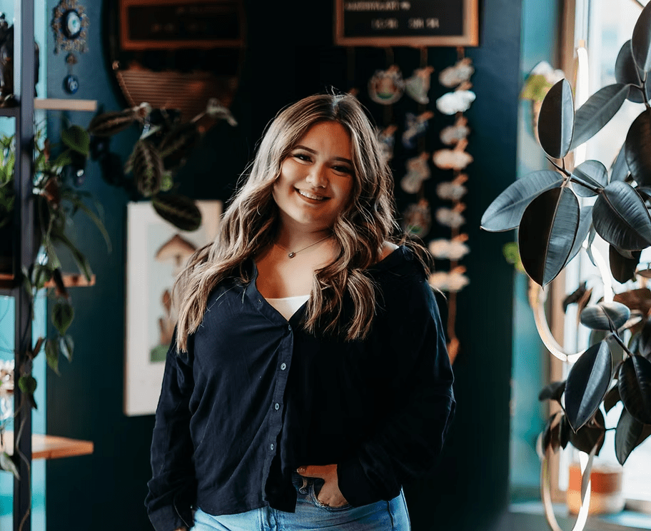 A woman is standing in a room with plants and smiling.