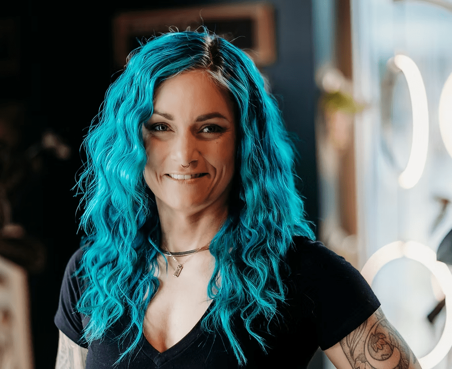 A woman with blue hair is wearing a black shirt and smiling.