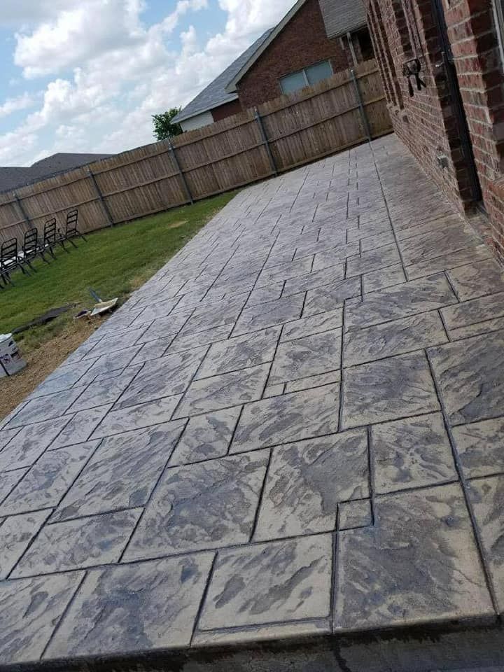 A concrete patio in front of a brick house with a fence in the background.