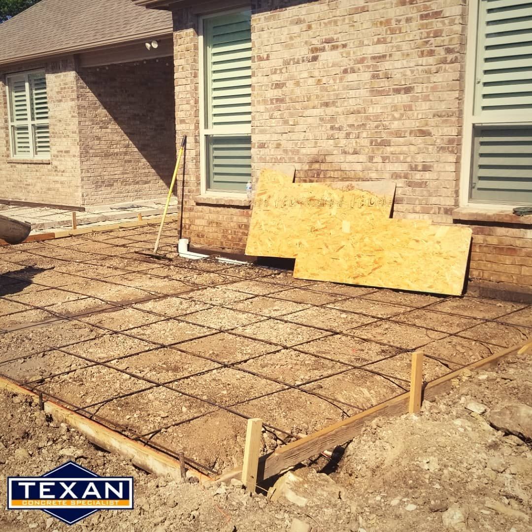 A concrete patio is being built in front of a brick house.