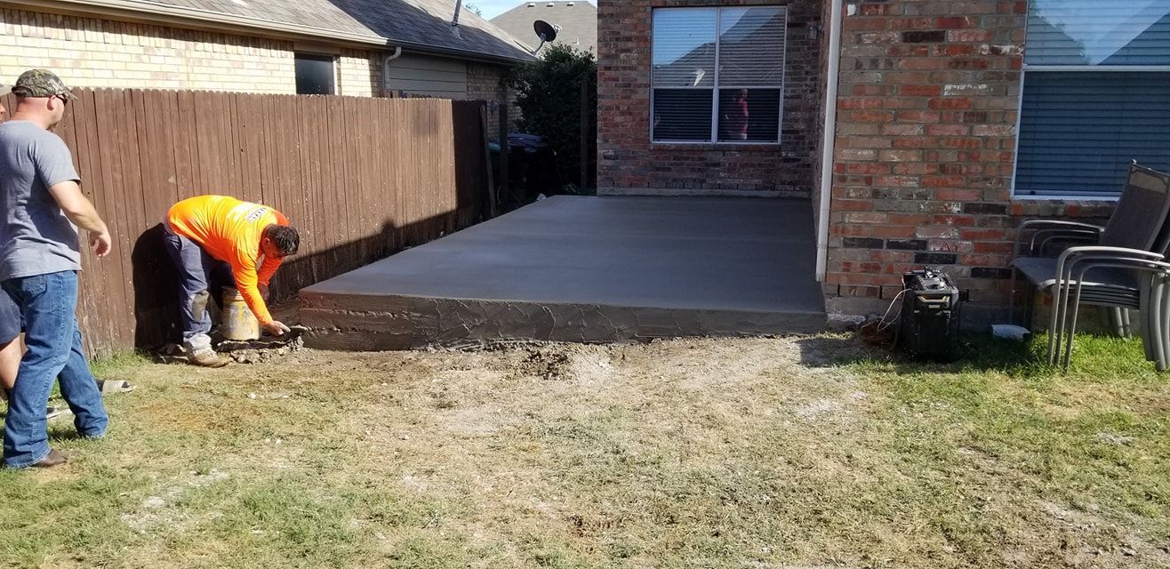Two men are working on a concrete patio in a backyard.