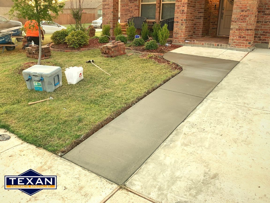 A concrete walkway is being built in front of a brick house.