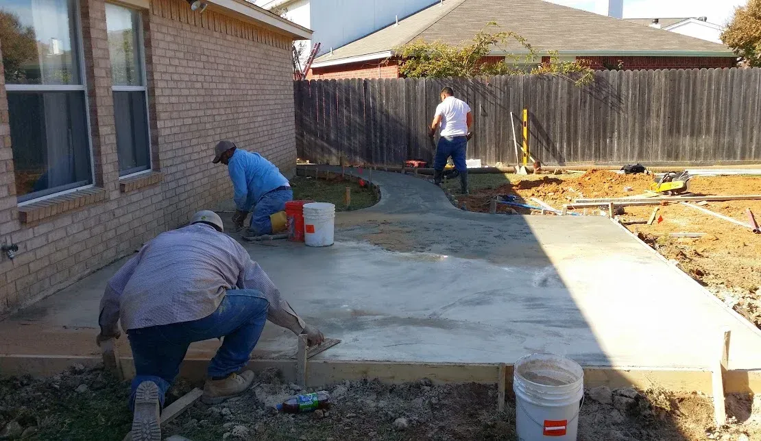 A group of men are working on a concrete walkway in front of a house.