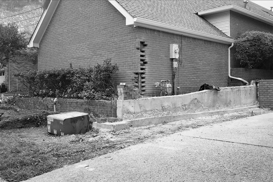 A black and white photo of a house with a concrete wall in front of it.