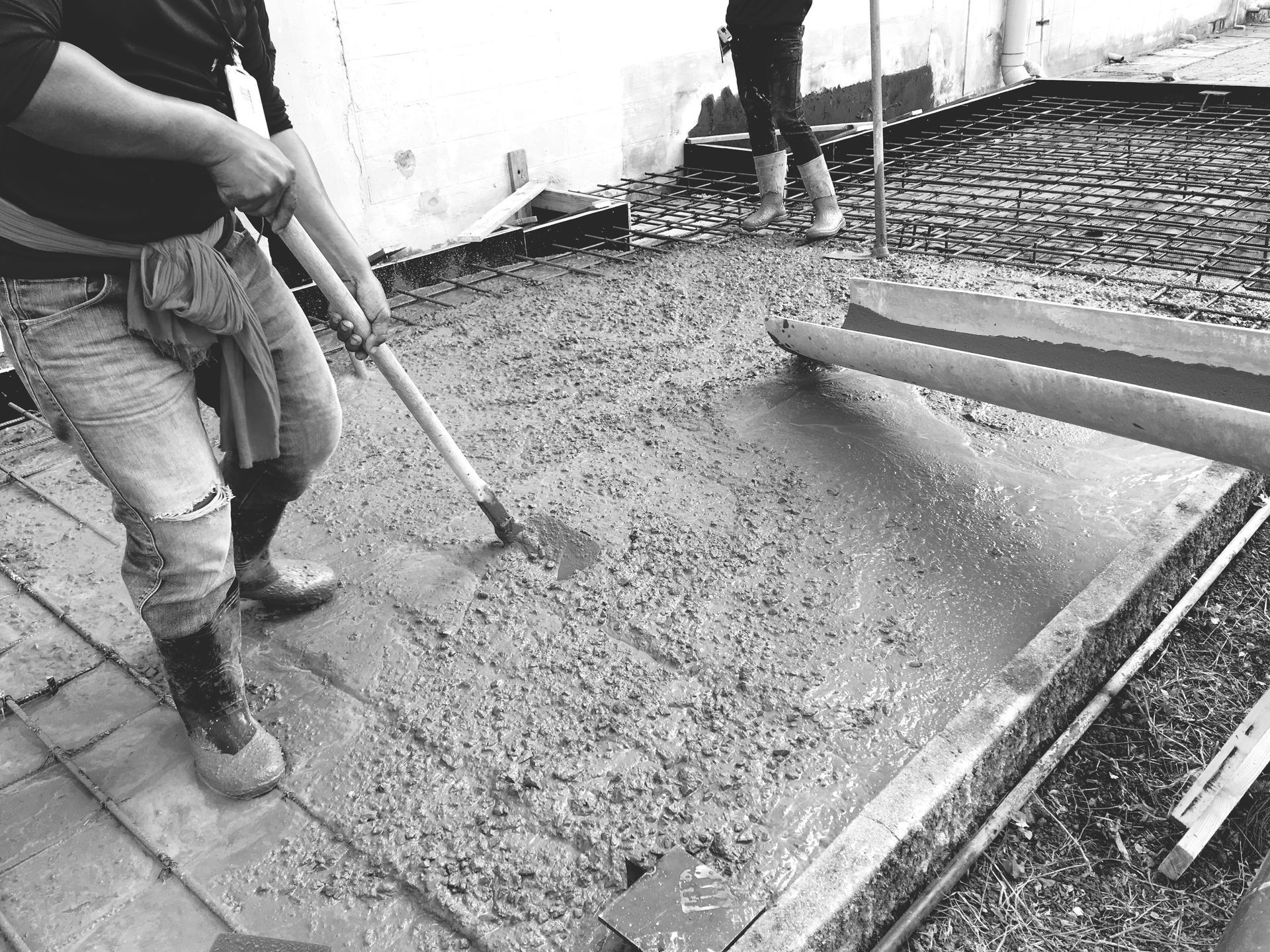 A black and white photo of a man pouring concrete on a sidewalk.