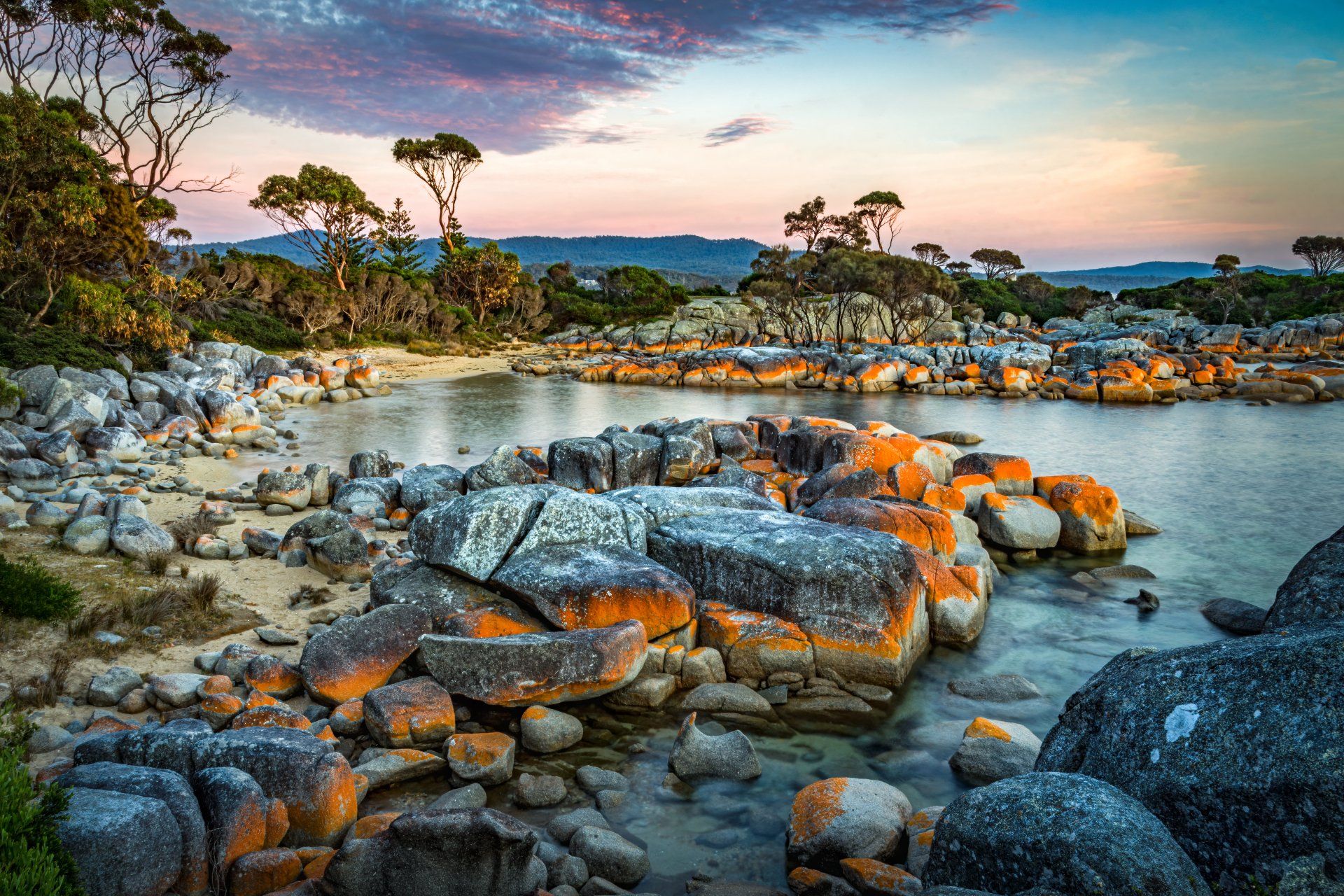 Body of water surrounded by rocks and trees with a sunset in the background