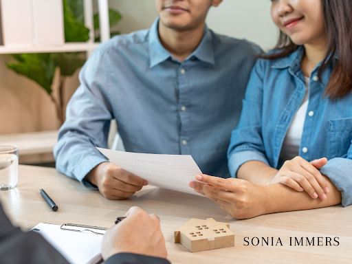 Couple reviewing paperwork with an agent, a model house on the table.