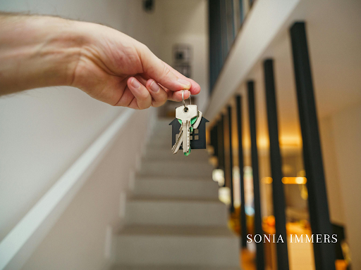 Hand holding keys with house-shaped keychain near a staircase.