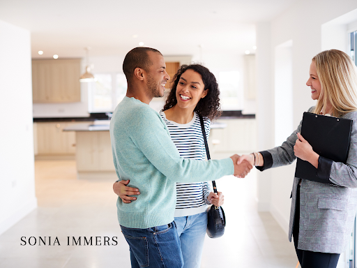 Couple shaking hands with a real estate agent in an open-concept house.