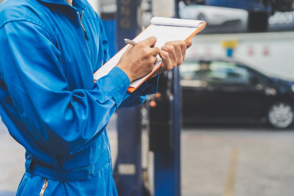 A Man in A Blue Jumpsuit Is Holding a Clipboard and Writing on It — Pacific Plaza Automotive in Port Macquarie, NSW