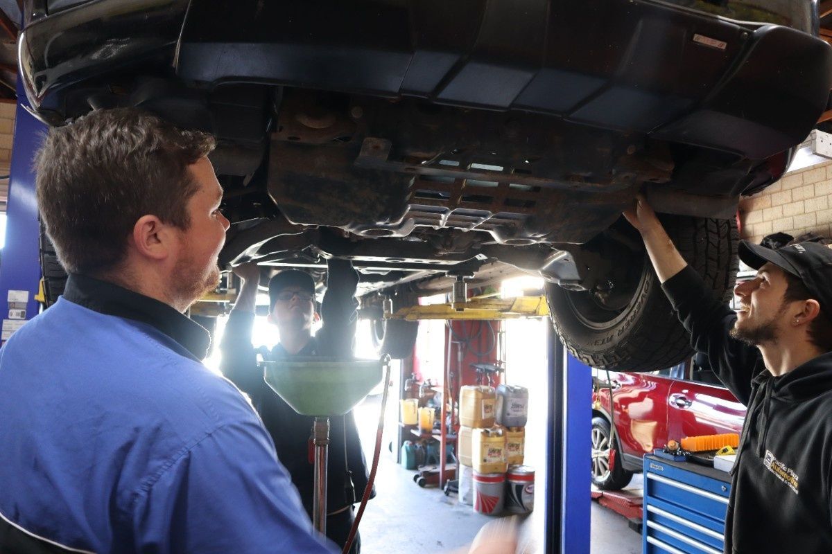 Three men are working under a car in a garage — Pacific Plaza Automotive in Port Macquarie, NSW