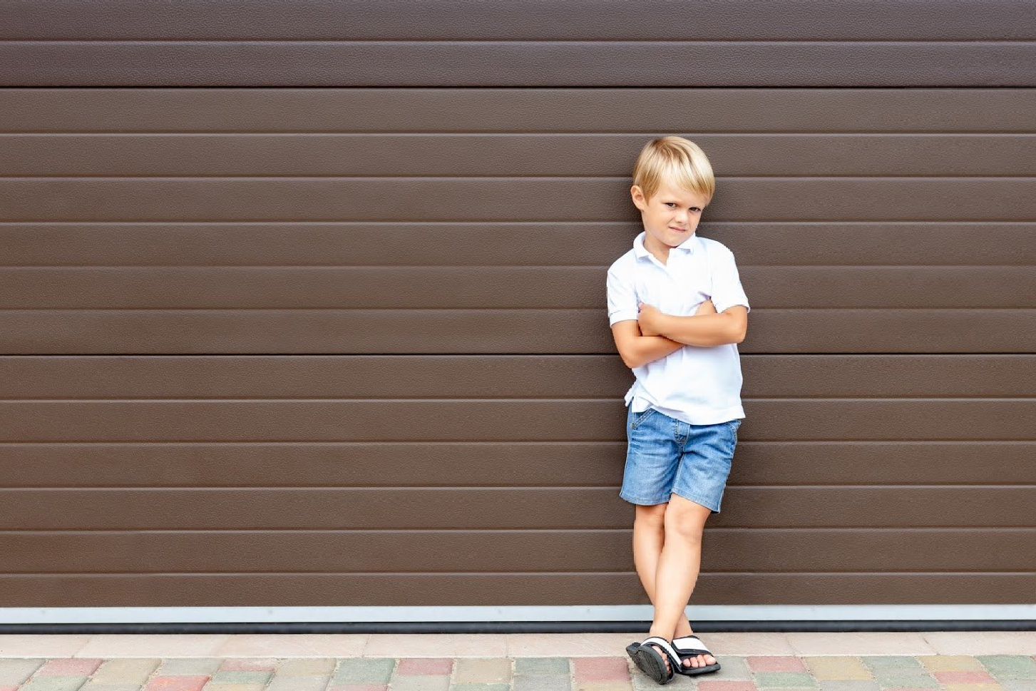 A Young Boy Is Standing in Front of A Garage Door with His Arms Crossed - Rochester Hills, MI - J & B Doors