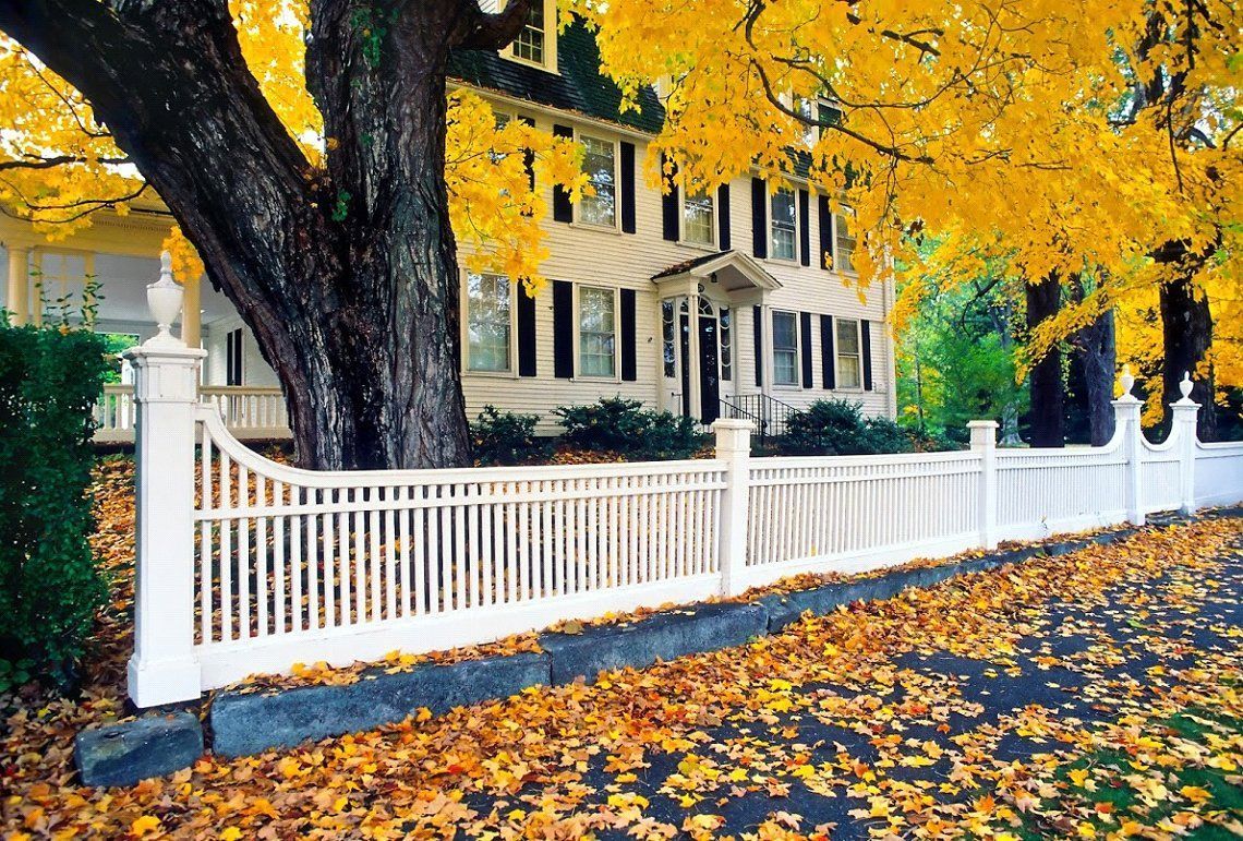 A White Fence Surrounds a House with Yellow Leaves on The Ground - Rochester Hills, MI - J & B Doors