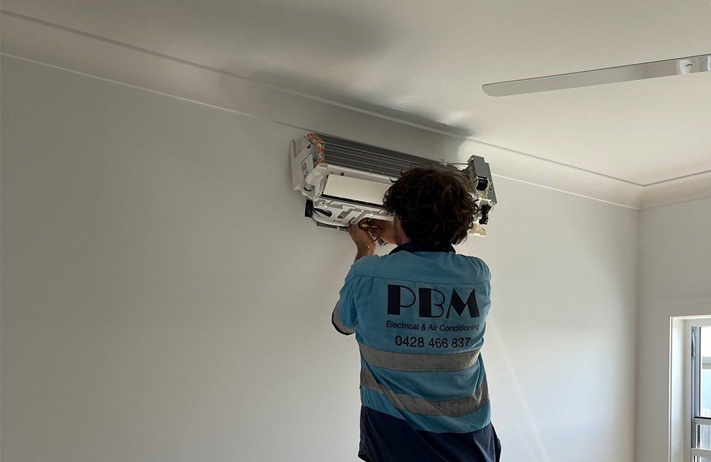 A Professional Installing An Air Conditioner — Electricians in the Whitsundays, QLD