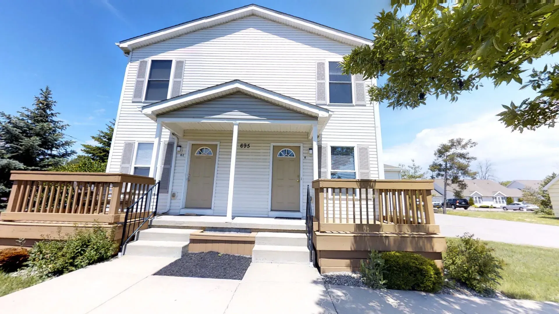 A white house with two doors and a wooden deck.