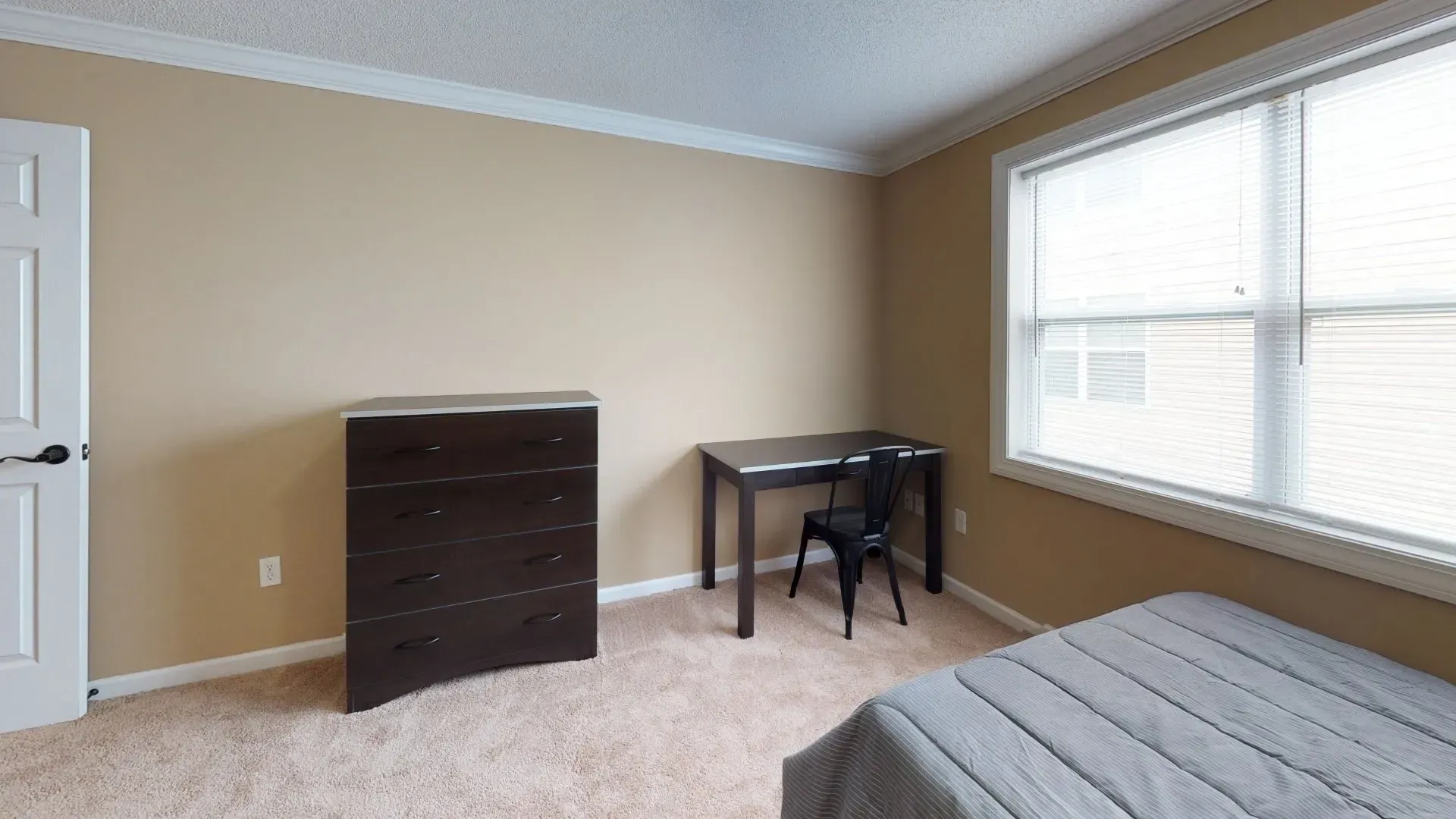 A bedroom with a bed , desk , chair and dresser.