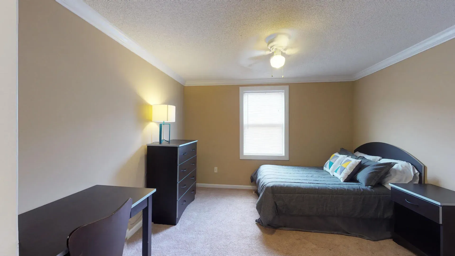 A bedroom with a bed , desk , dresser and window.