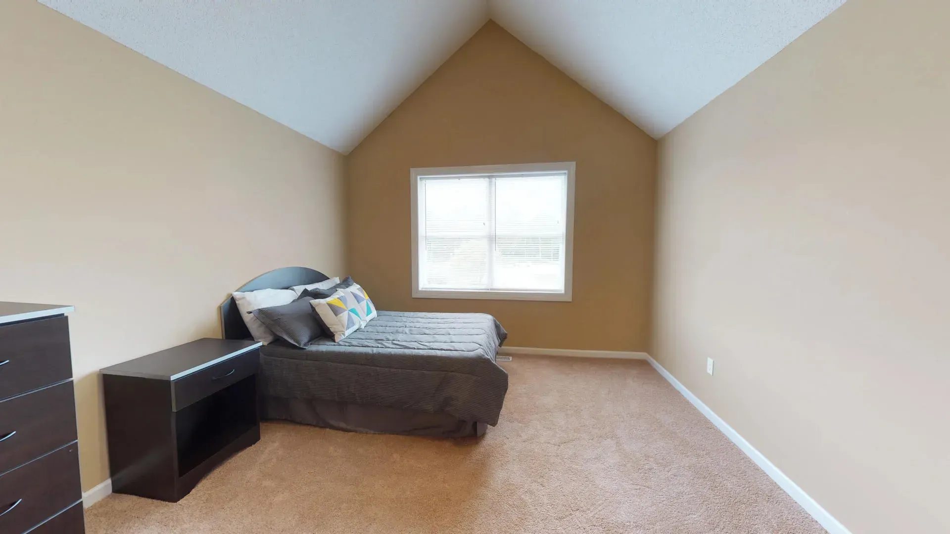 A bedroom with a bed , dresser , nightstand and window.