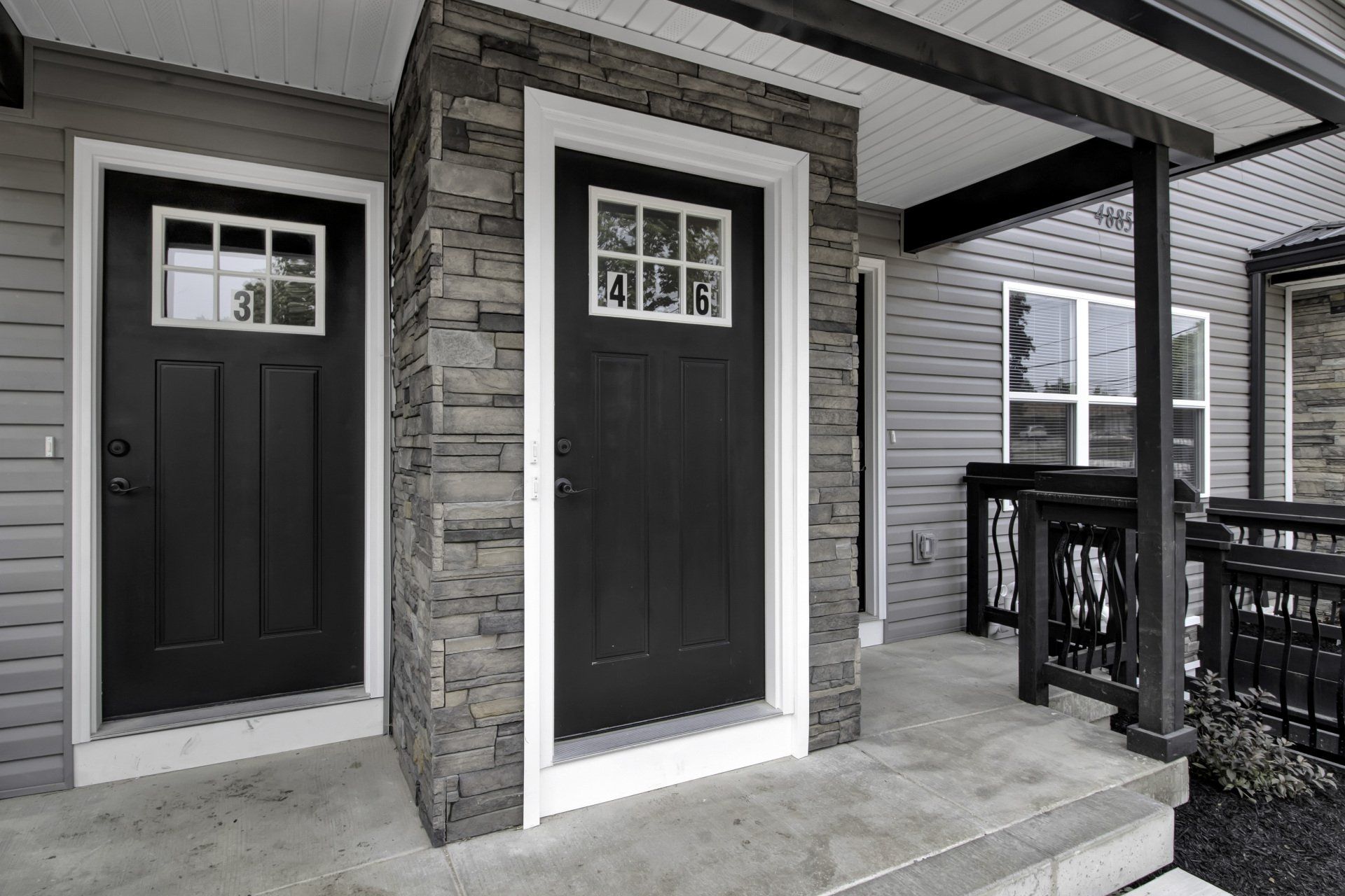 A black and white photo of a house with two black doors and a porch.