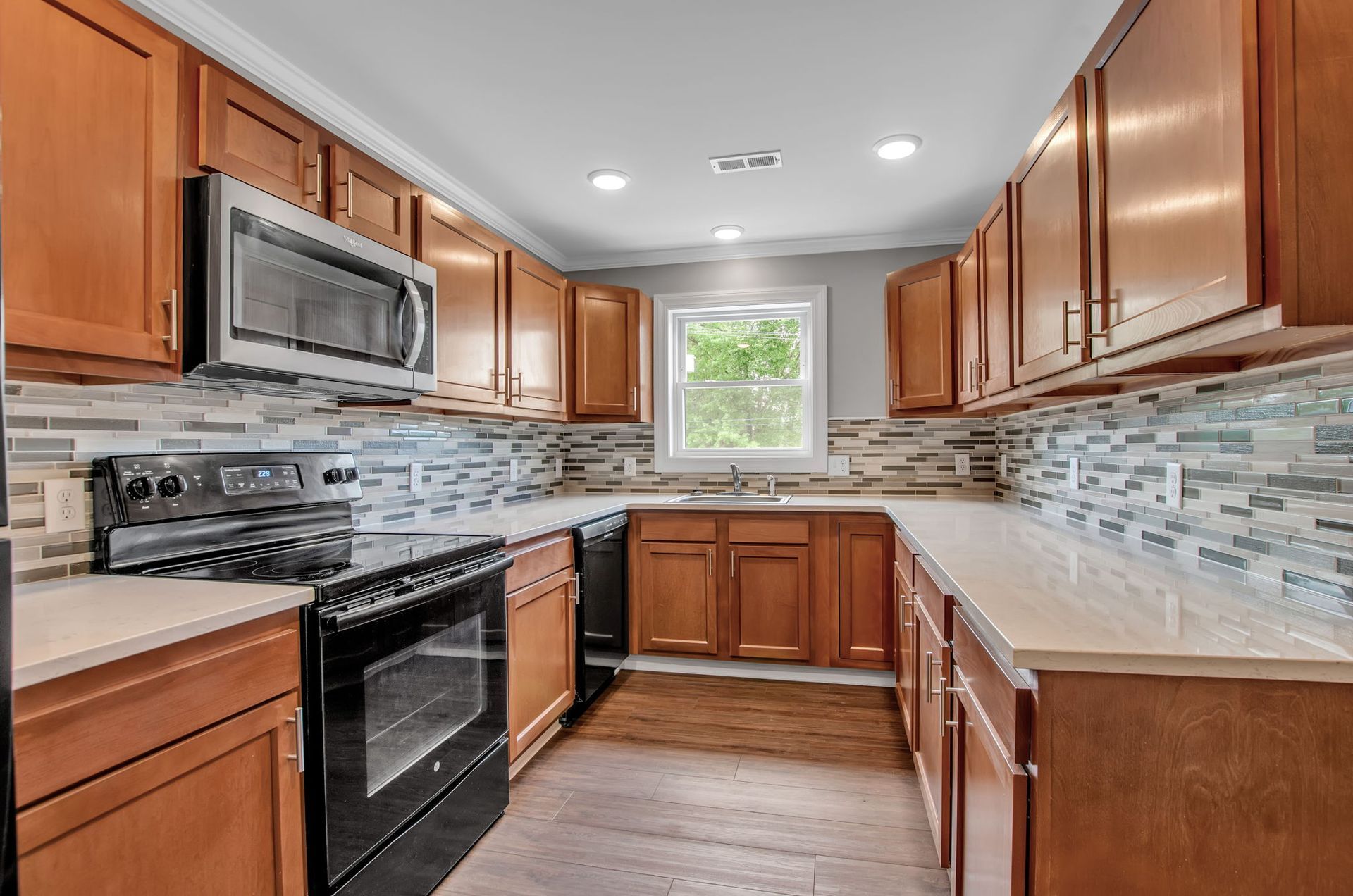 A kitchen with wooden cabinets , a black stove , a microwave , and a window.