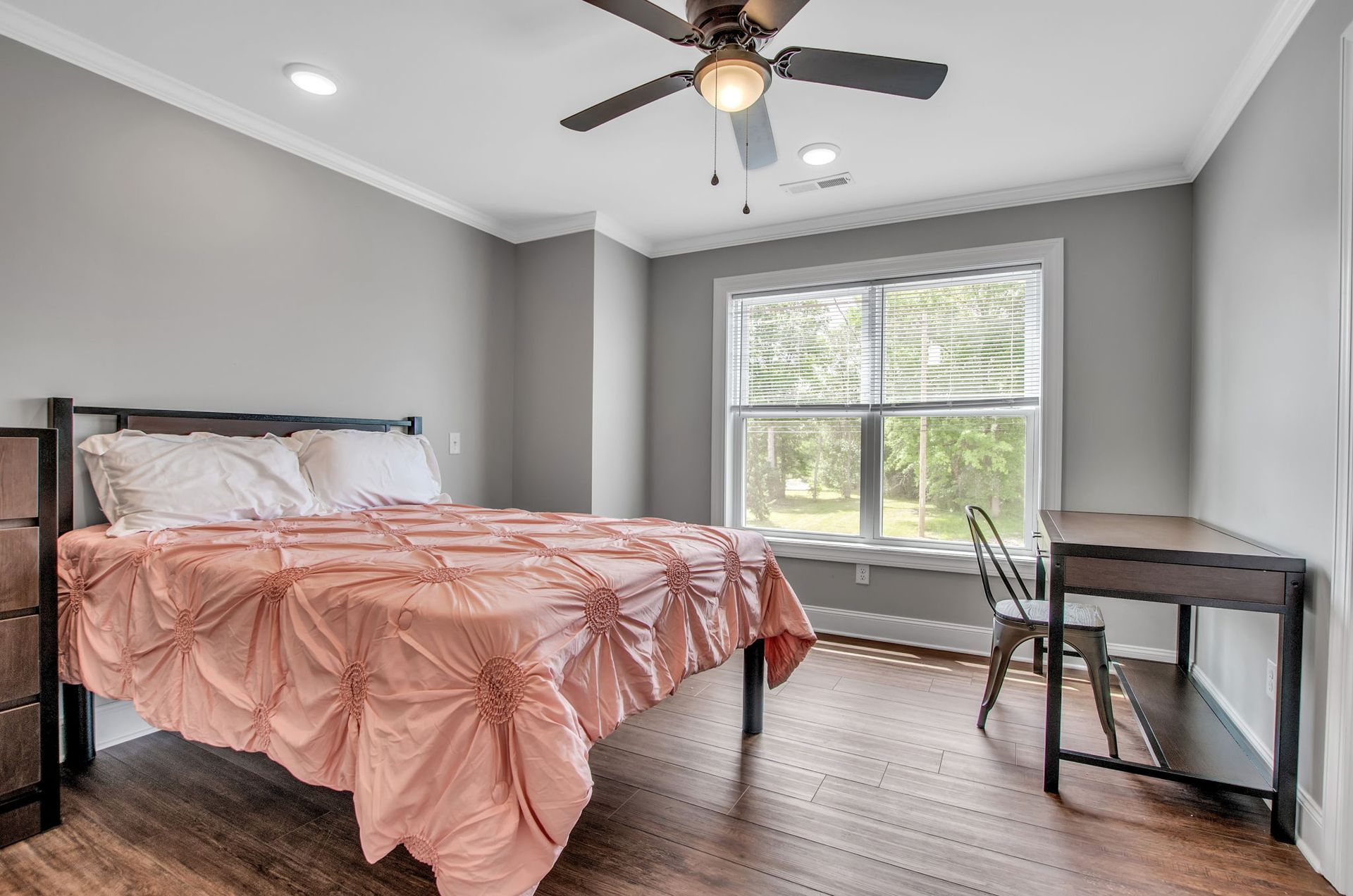 A bedroom with a bed , desk , chair and ceiling fan.
