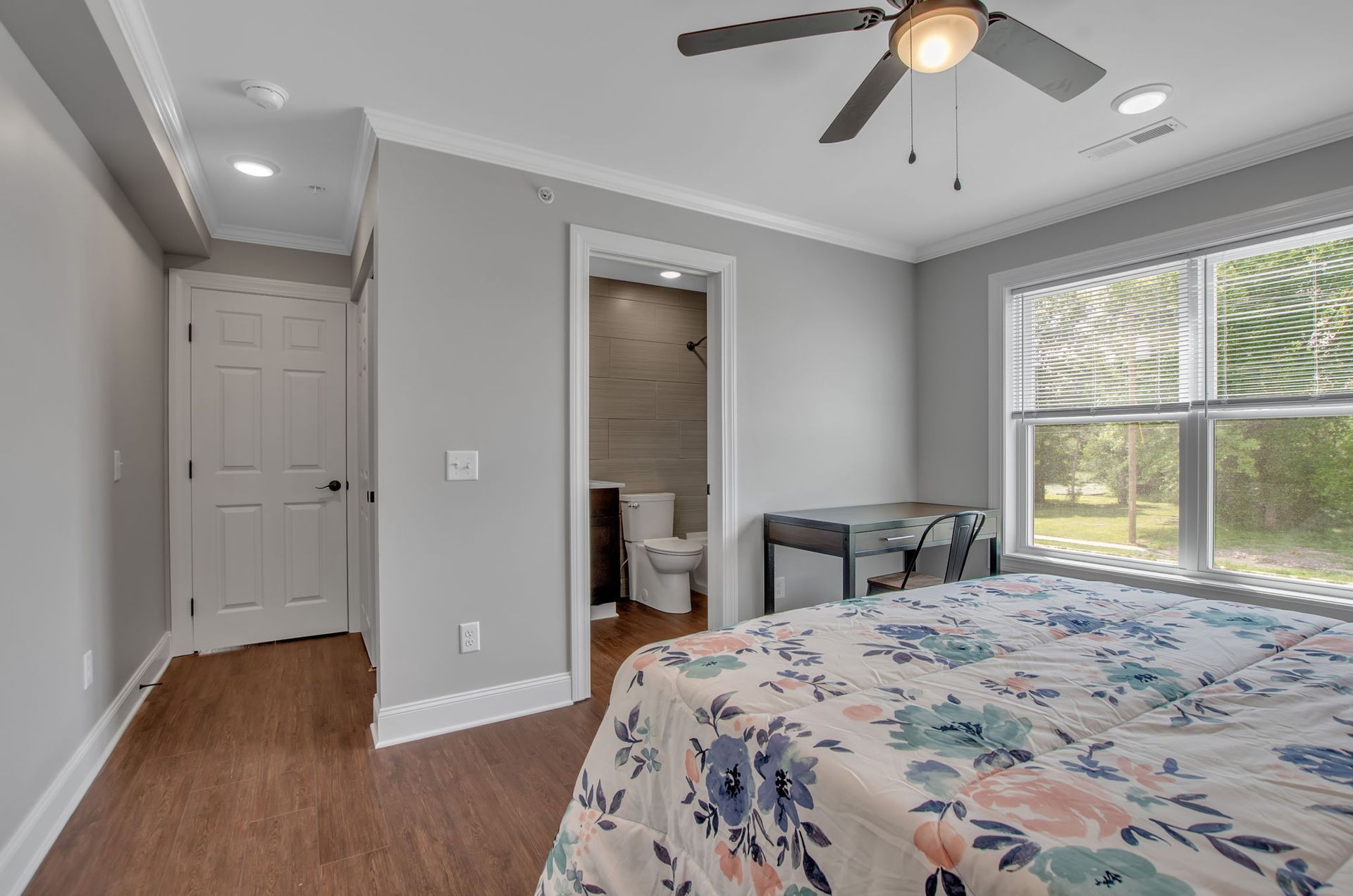 A bedroom with a bed , ceiling fan , toilet and window.