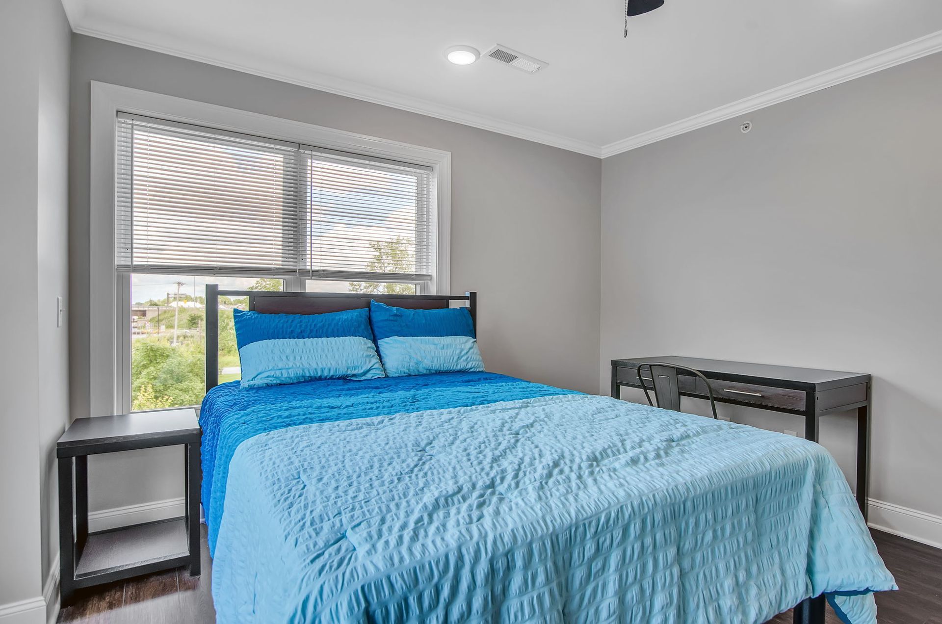 A bedroom with a bed , nightstand , desk and window.