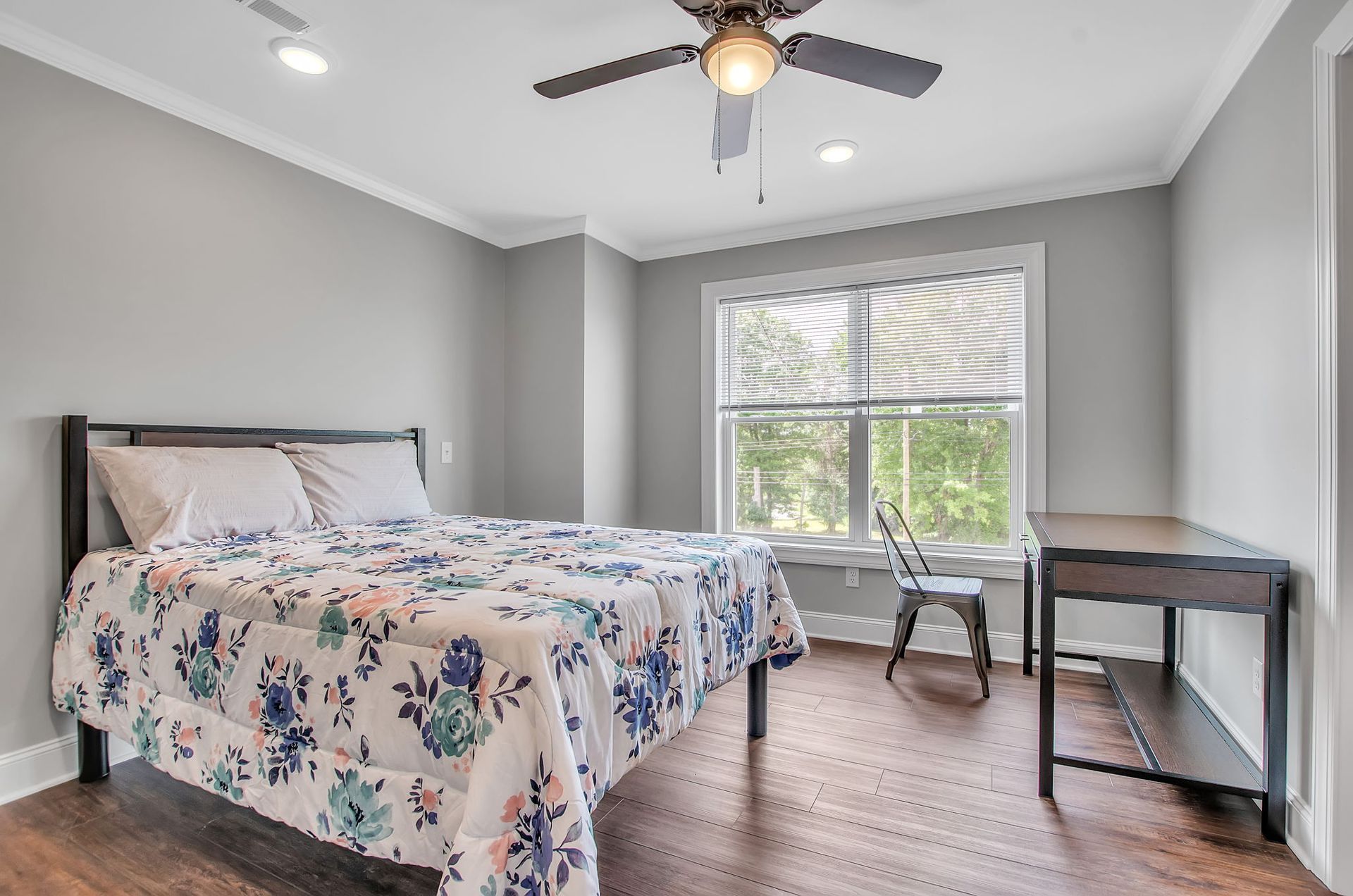 A bedroom with a bed , desk , chair and ceiling fan.
