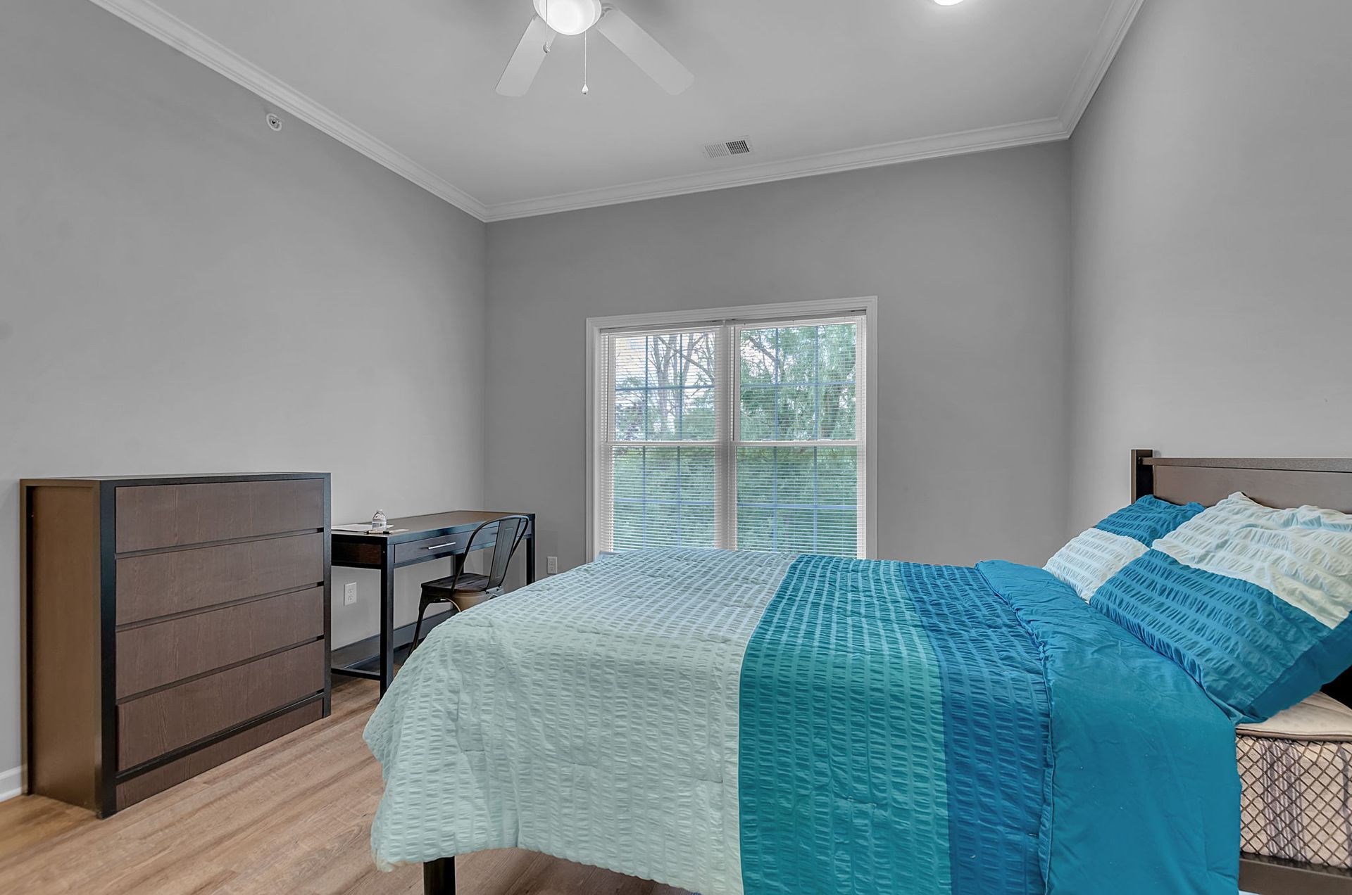 A bedroom with a bed , dresser , desk and ceiling fan.