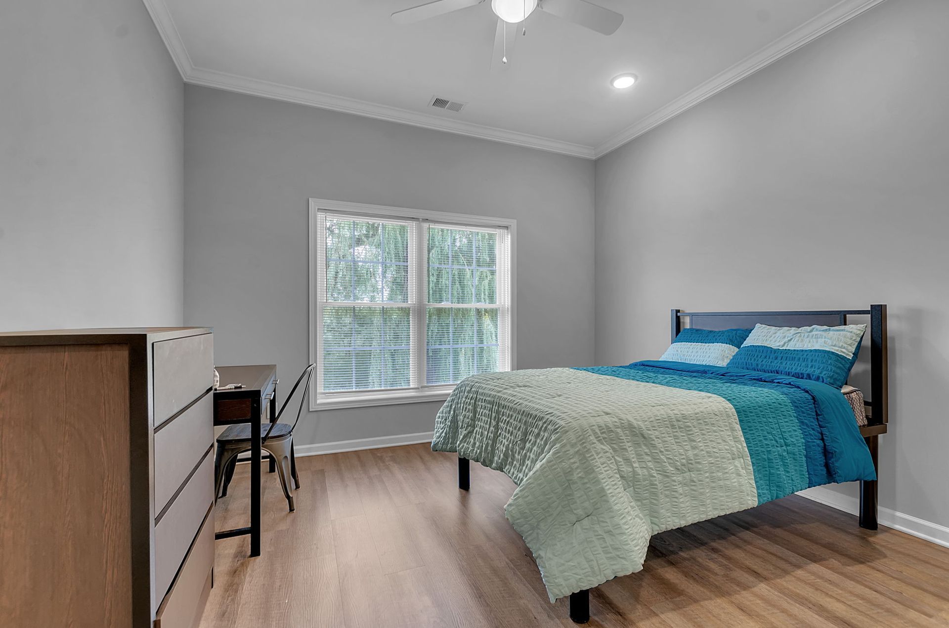 A bedroom with a bed , desk , dresser and window.