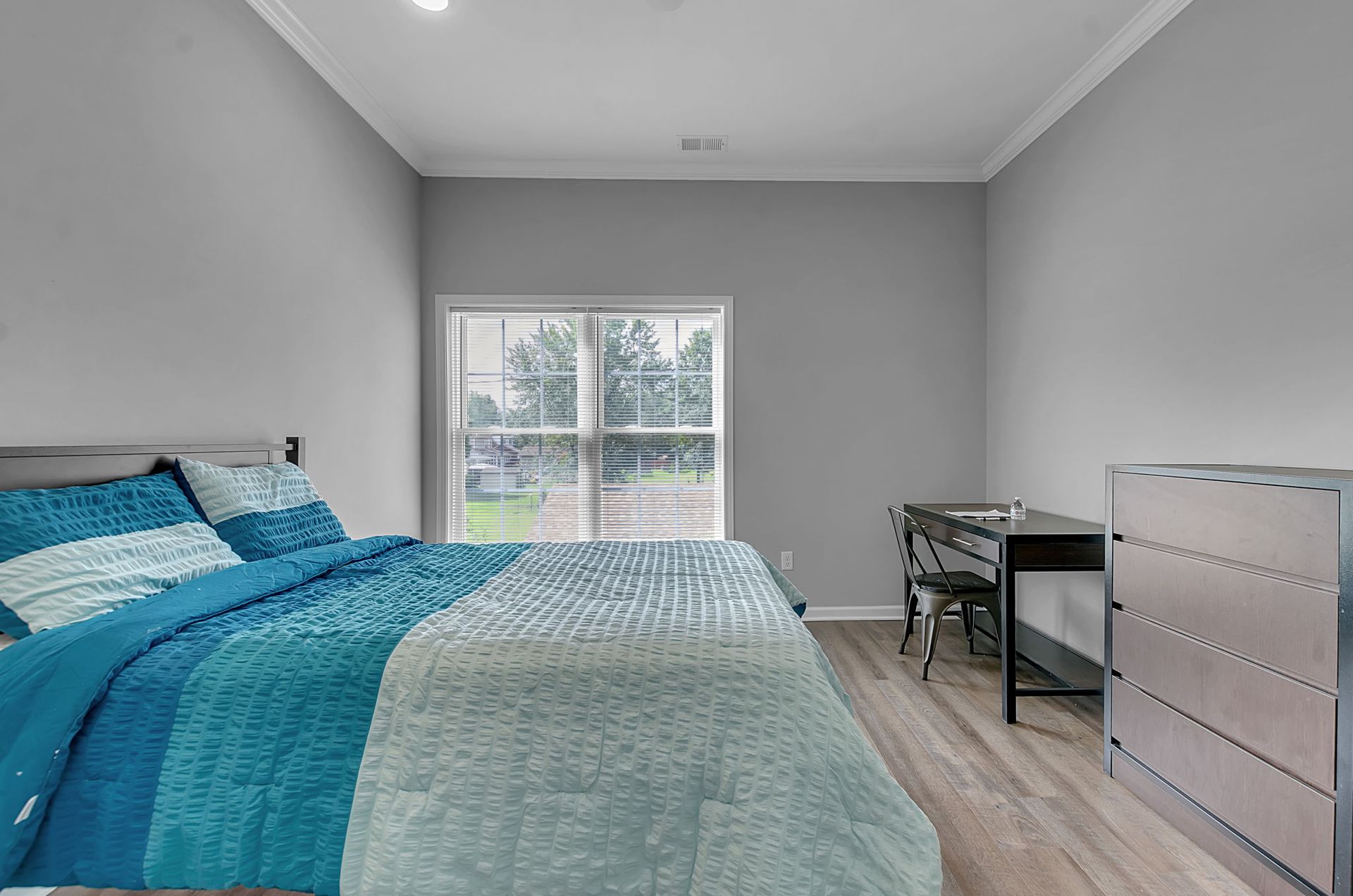 A bedroom with a bed , desk , dresser and sliding glass door.