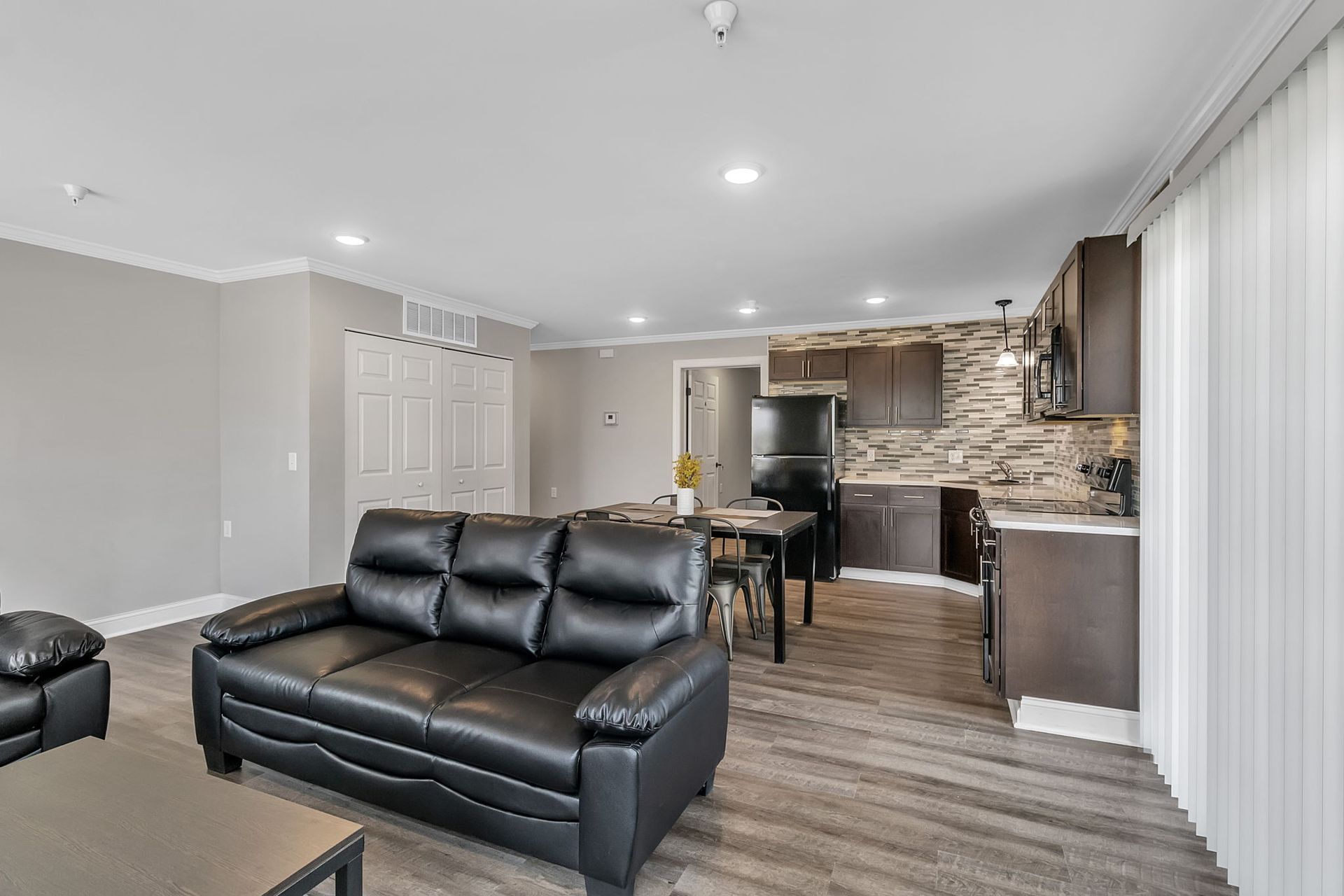 A living room with a black couch and a kitchen in the background.