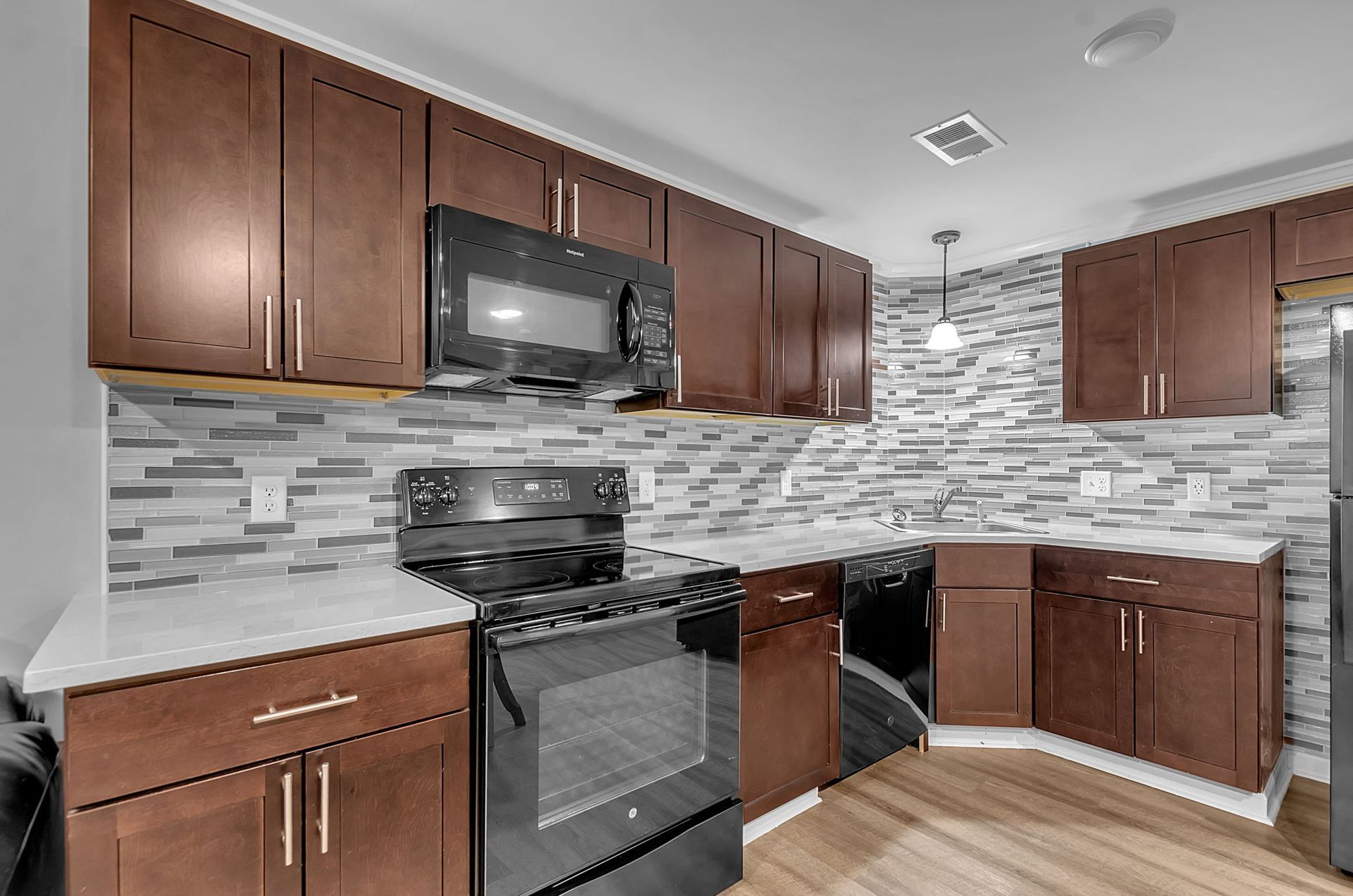 A kitchen with wooden cabinets , black appliances , a stove , microwave and refrigerator.