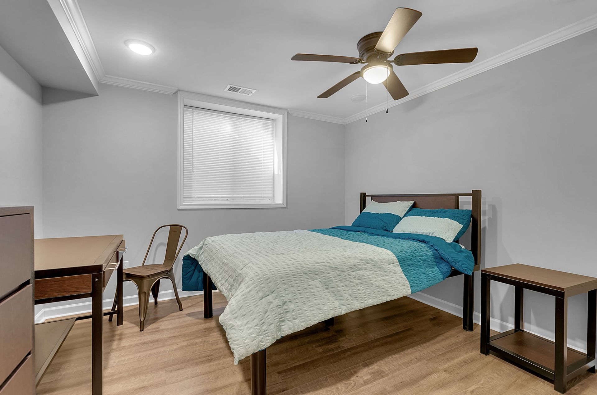 A bedroom with a bed , nightstand , desk and ceiling fan.