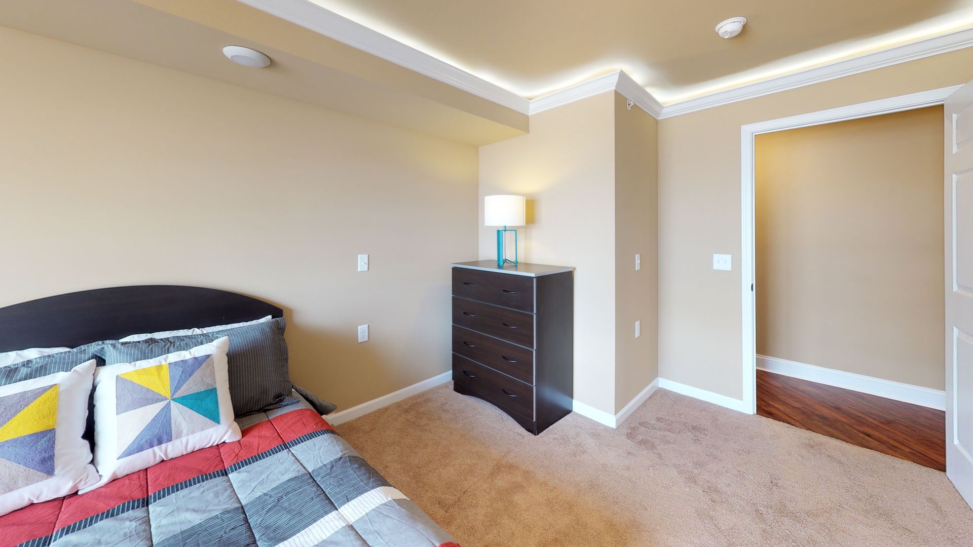 A bedroom with a bed , dresser , lamp and a walk in closet.