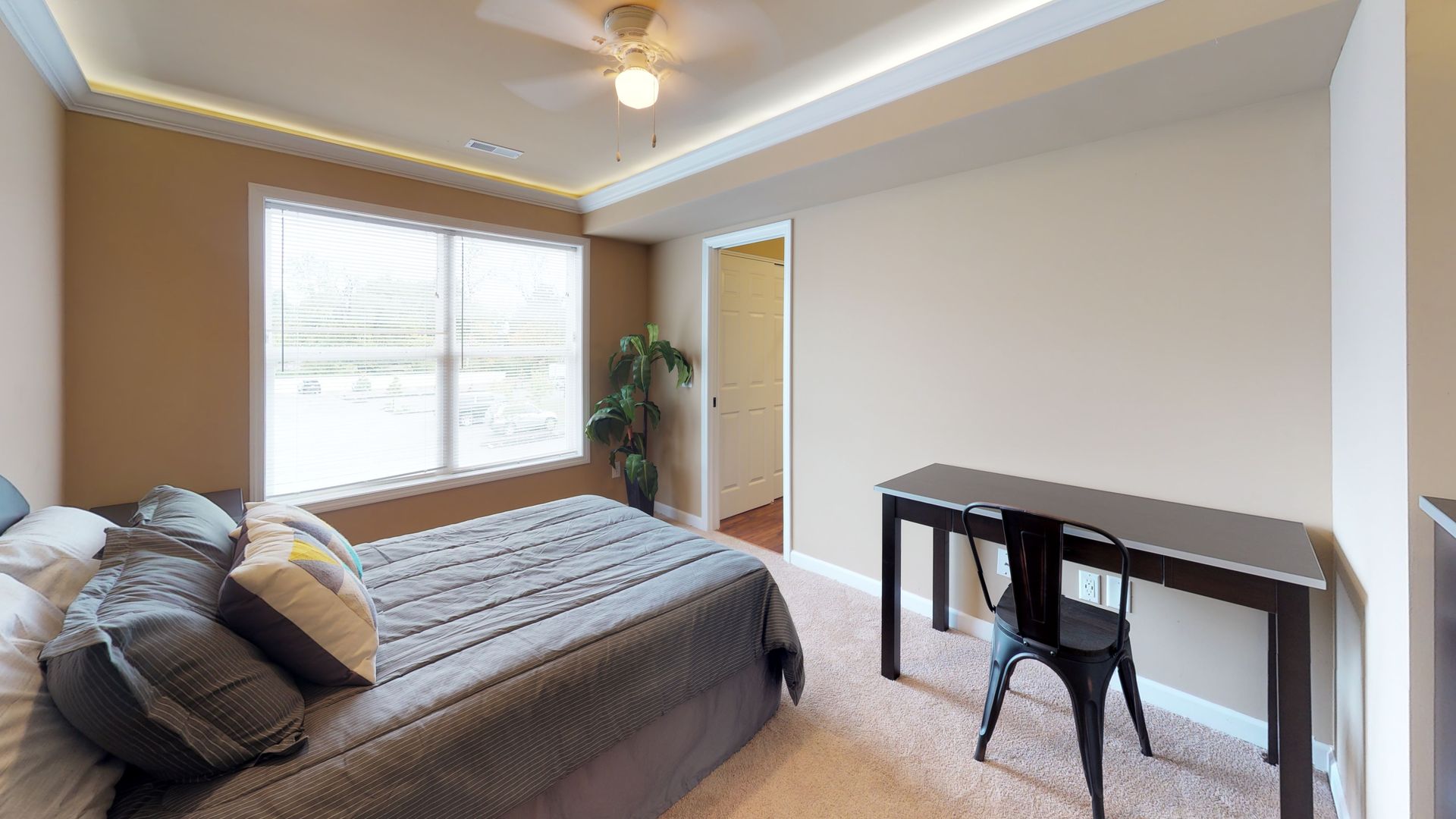 A bedroom with a bed , desk , chair and ceiling fan.