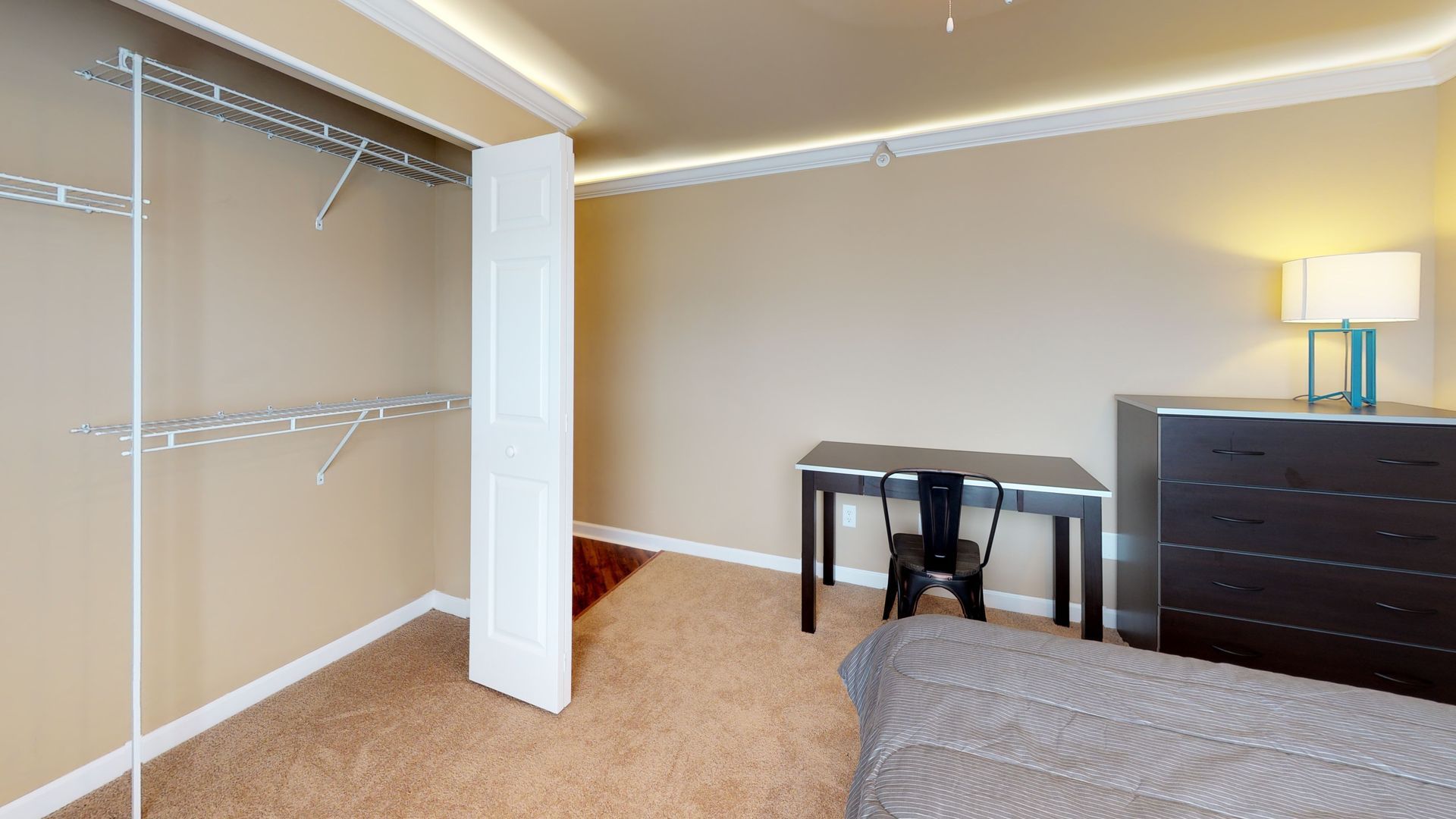 A bedroom with a bed , desk , dresser and walk in closet.
