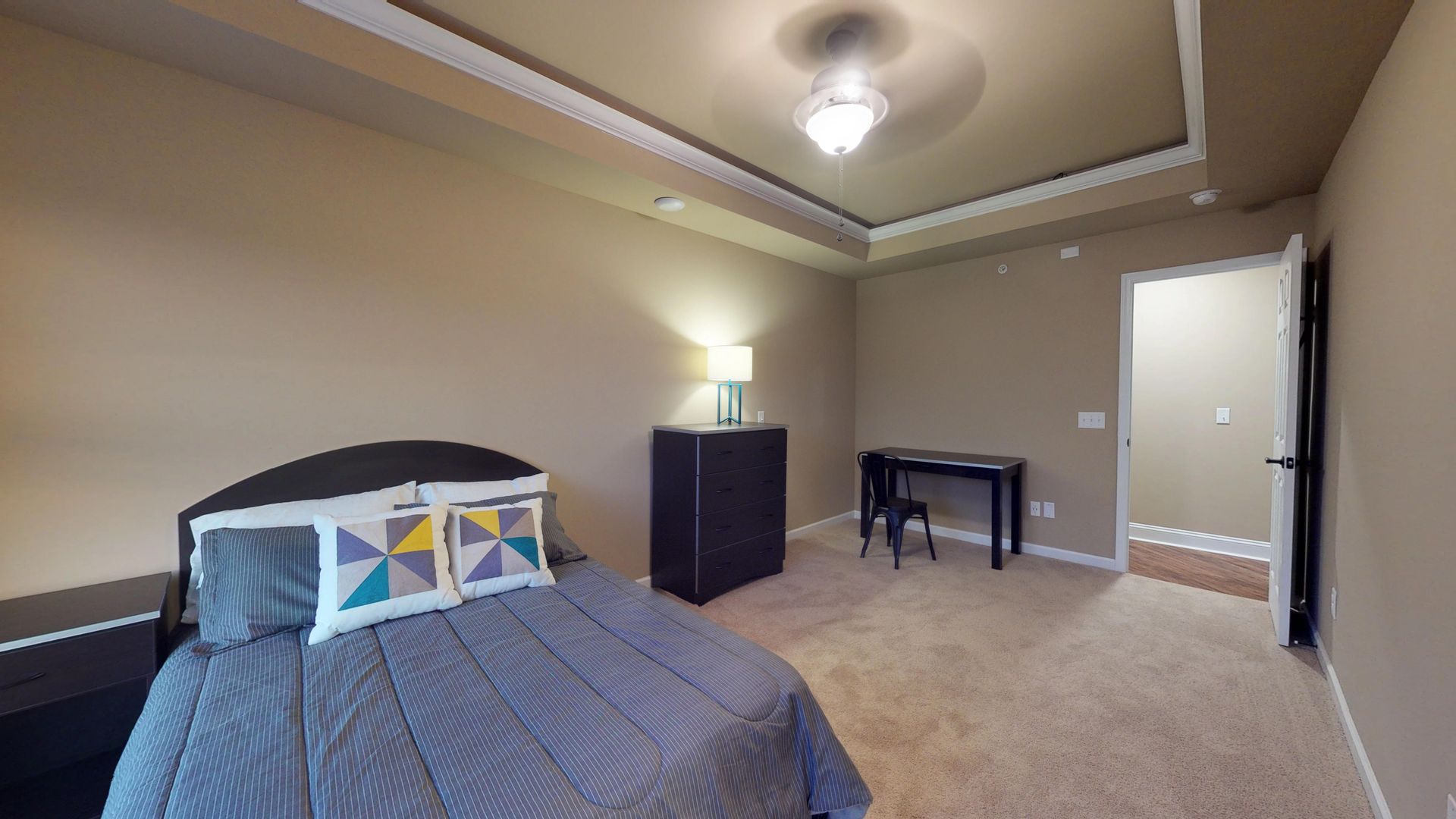 A bedroom with a bed , desk , nightstand and ceiling fan.