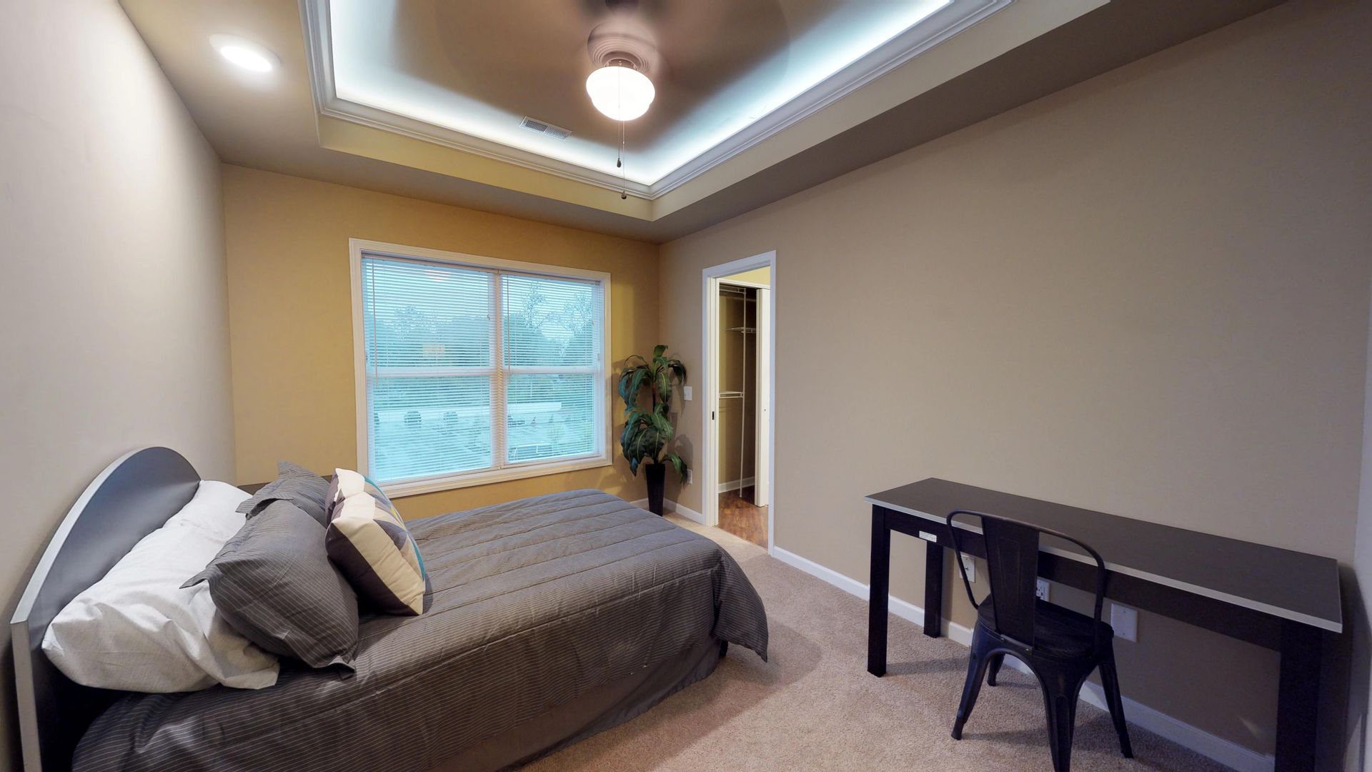 A bedroom with a bed , desk , chair and ceiling fan.