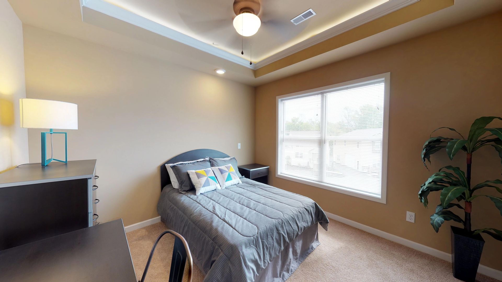 A bedroom with a bed , desk , lamp and window.