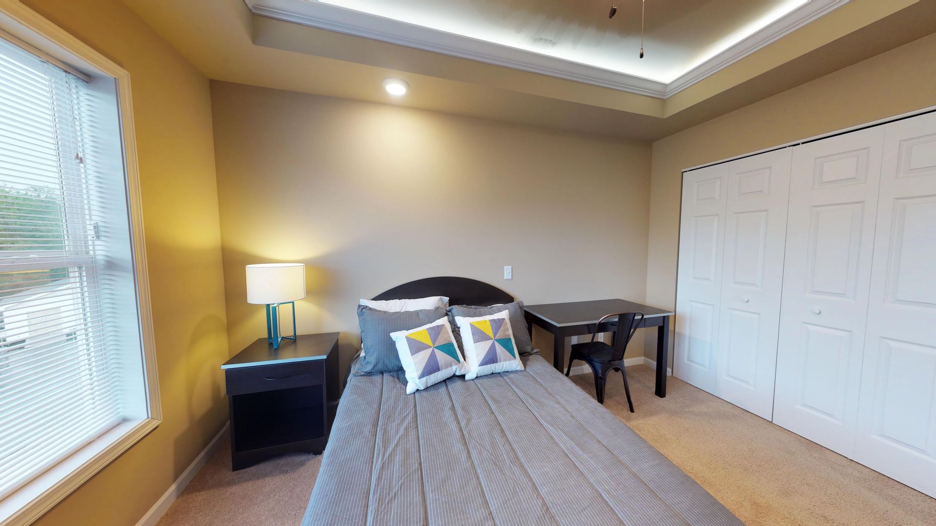 A bedroom with a bed , nightstand , desk and window.