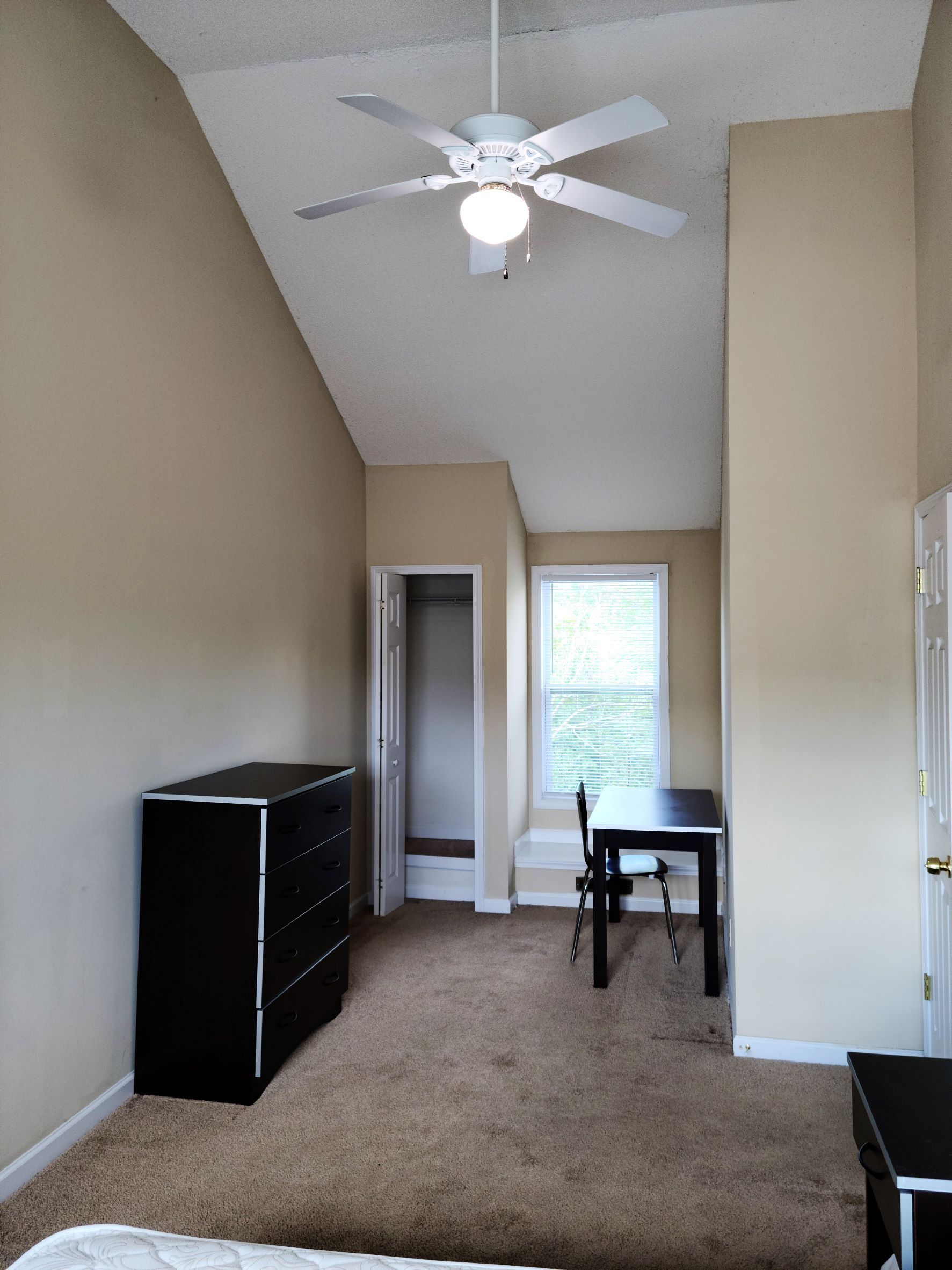 A bedroom with a ceiling fan and a desk